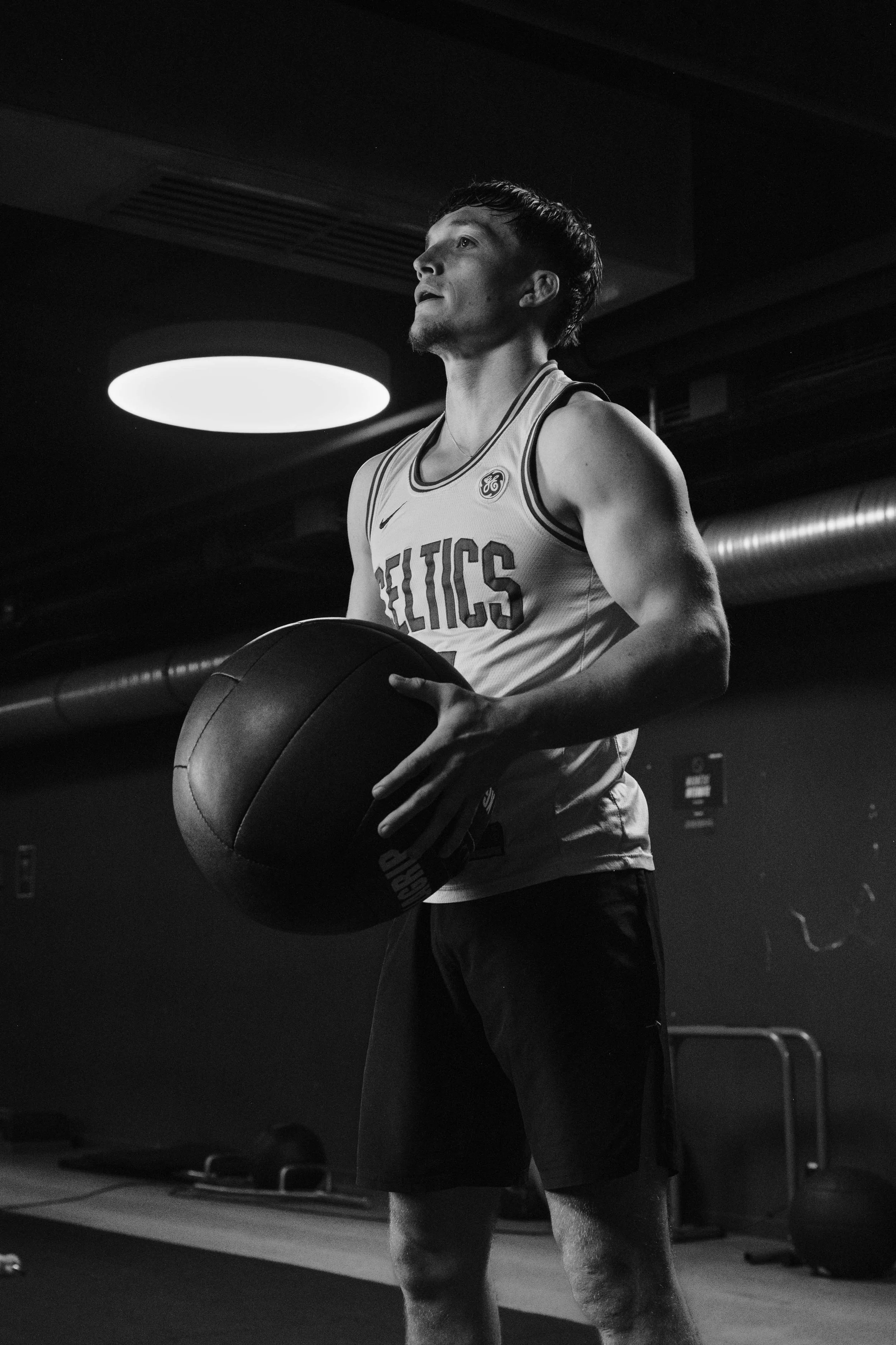 Un combattant de MMA en tenue des Celtics, tenant un ballon, dans une salle d'entraînement, en noir et blanc. Issue d'une vidéo de sport du Studio Kroma pour le projet Limitless.
