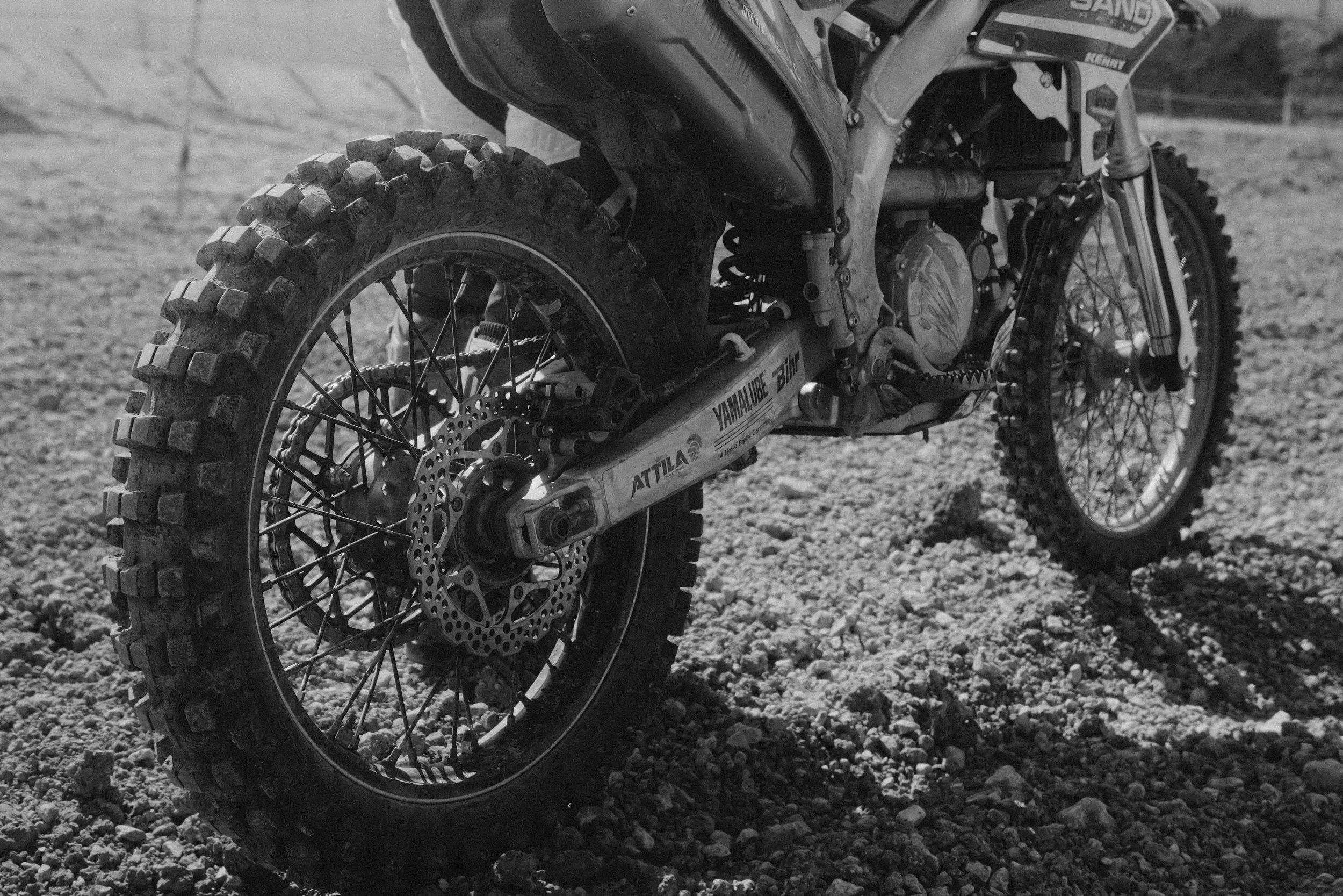 Une moto tout-terrain (motocross) sur un terrain de gravier, vue en gros plan du côté gauche, en noir et blanc. Issue d'une vidéo de sport du Studio Kroma pour le projet Limitless.