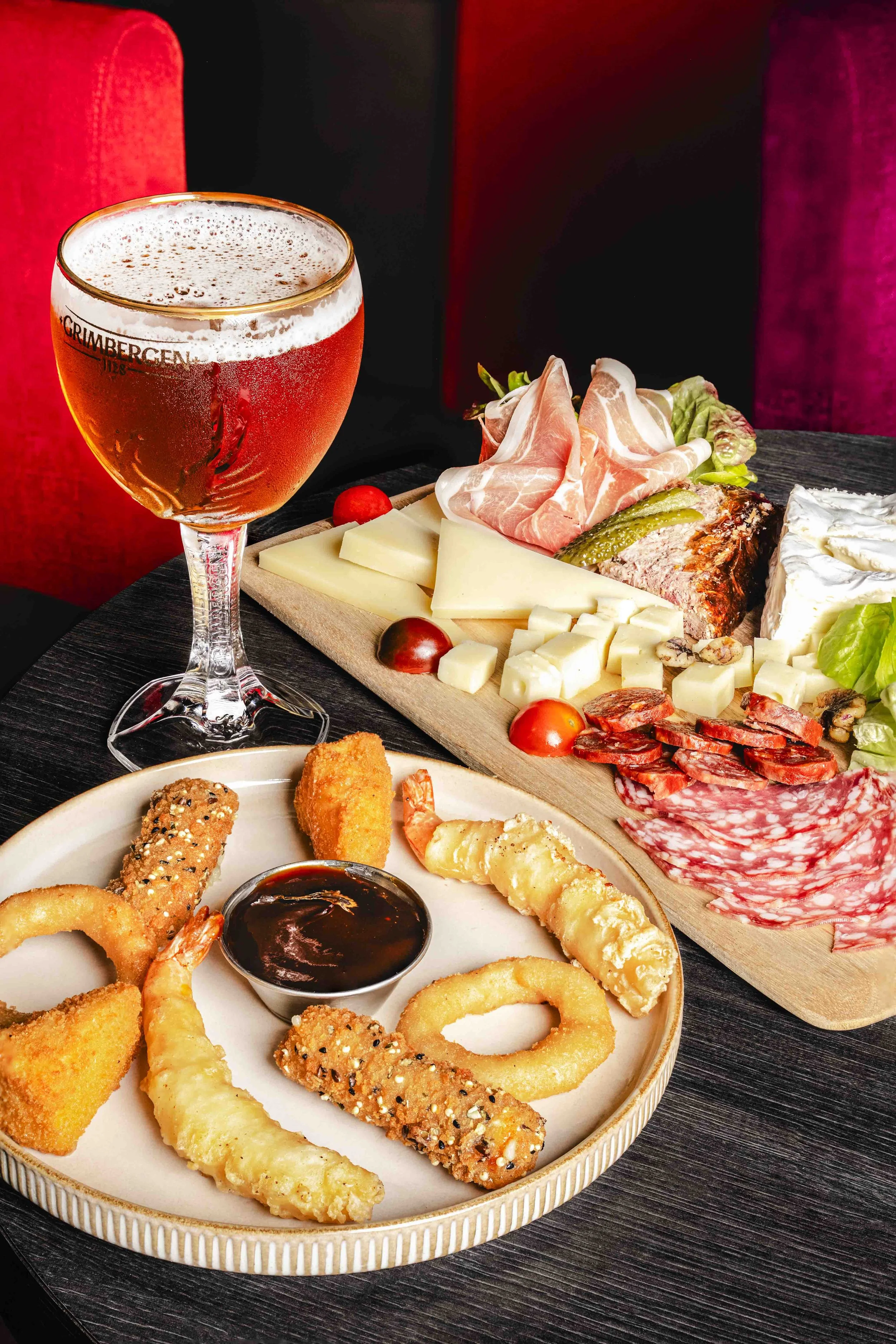 Plate de poissons frits avec sauce barbecue et une coupe de bière rosée en arrière-plan, accompagnée d'une planche de fromages, charcuterie et légumes. Contexte de restaurant ou de bar. Issue d'un projet de photo culinaire du Studio Kroma pour le re