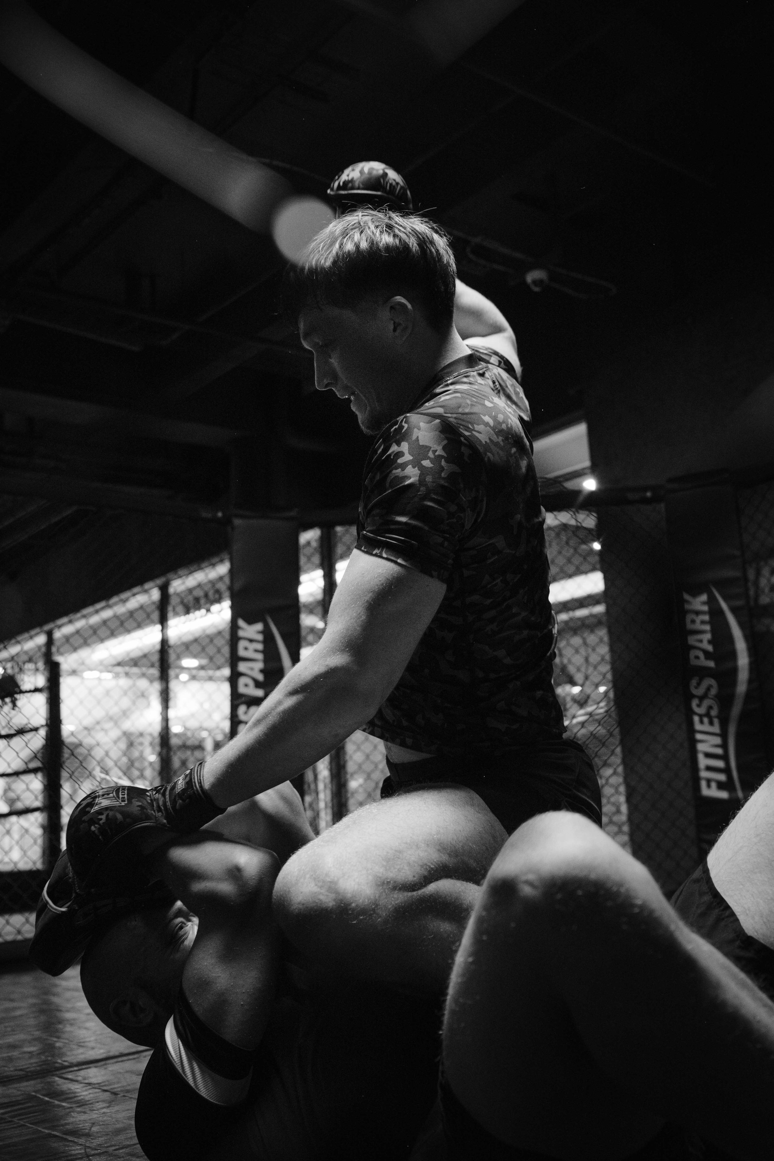 Deux hommes pratiquent un combat de MMA dans une cage d'entraînement, l'un au sol et l'autre en position de domination. Issue d'une vidéo de sport du Studio Kroma pour le projet Limitless.