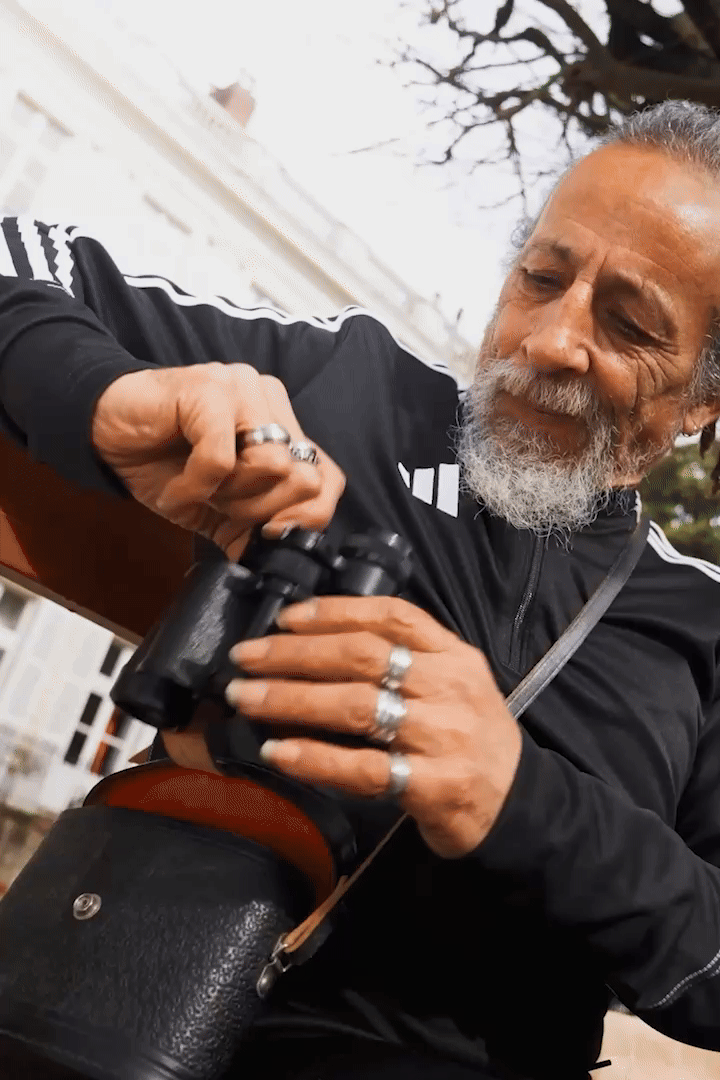 Un homme âgé portant un sweat noir regarde à travers une paire de jumelles.