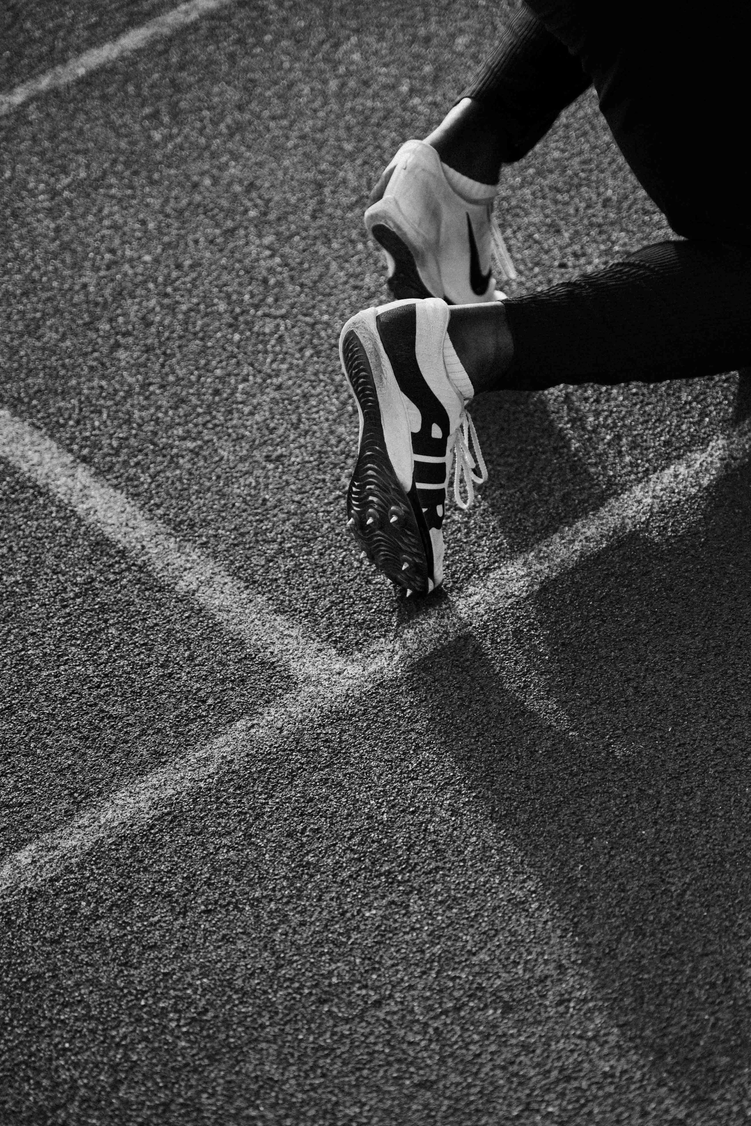 Une paire de chaussures de course sur une piste d'athlétisme, vue en gros plan en noir et blanc. Issue d'une vidéo de sport du Studio Kroma pour le projet Limitless.