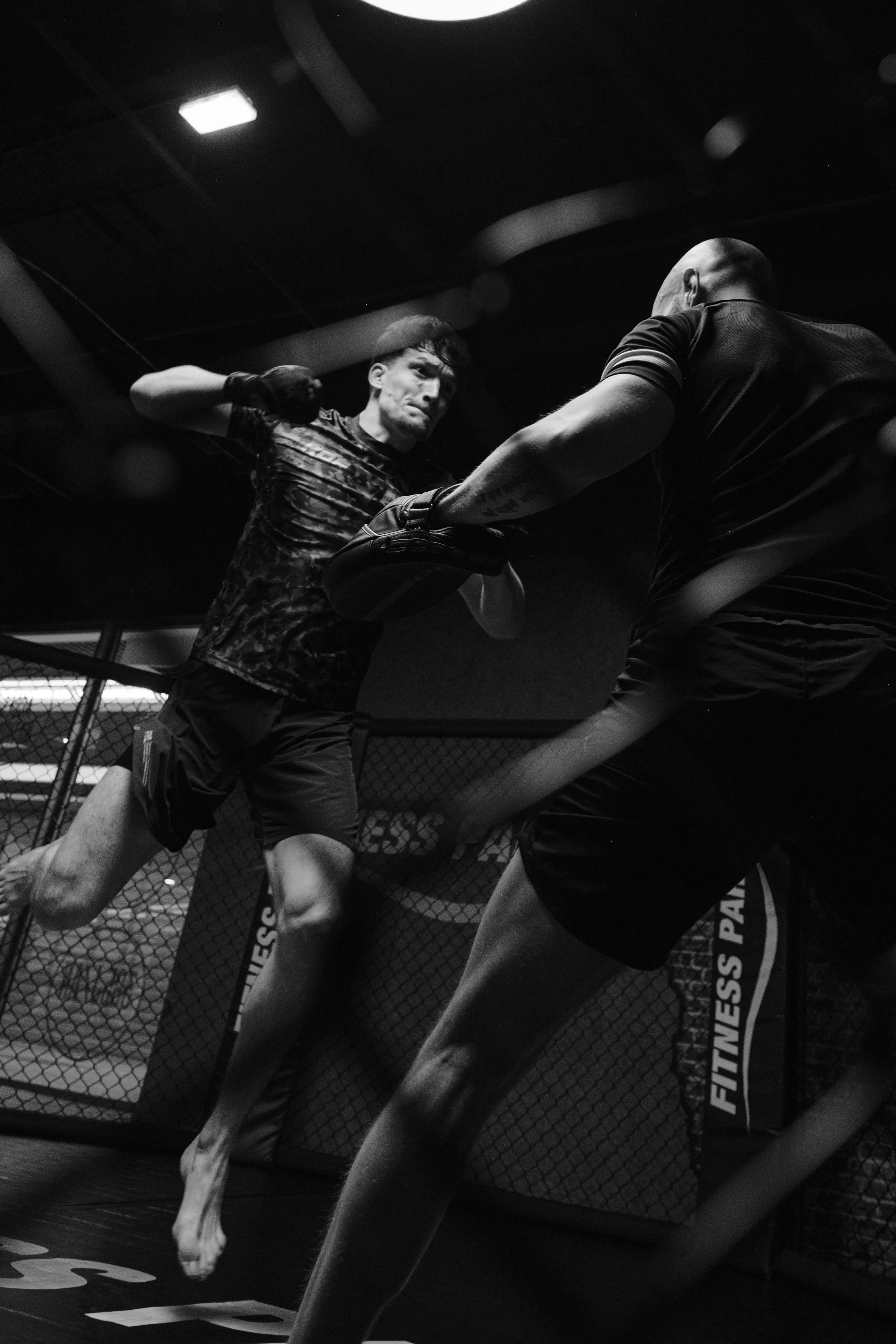 Deux hommes s'entraînent dans une cage de MMA, l'un donnant un coup de poing à l'autre. Issue d'une vidéo de sport du Studio Kroma pour le projet Limitless.