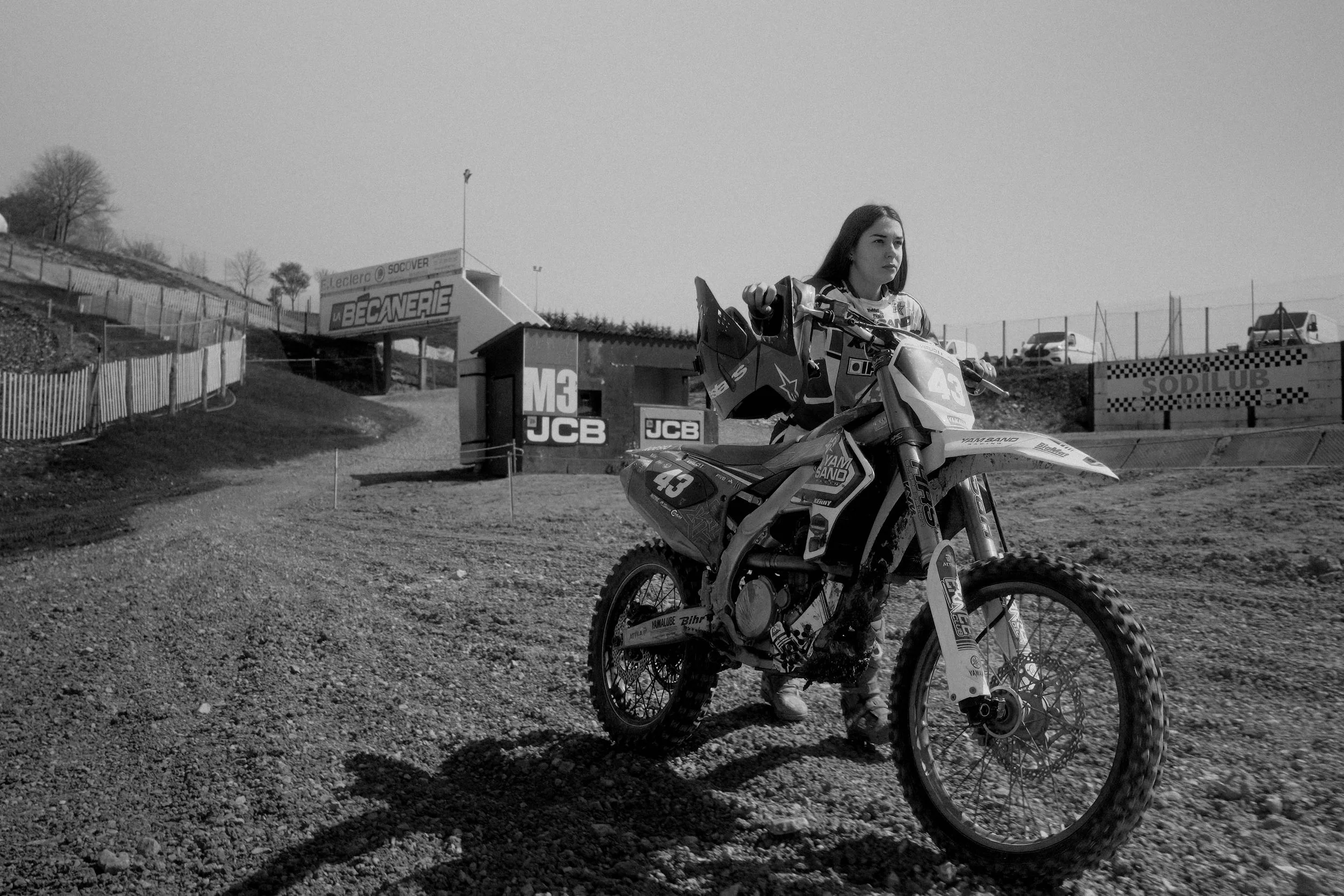 Une jeune femme avec une moto de motocross, se tenant sur un terrain poussiéreux à une piste de course. Issue d'une vidéo de sport du Studio Kroma pour le projet Limitless.
