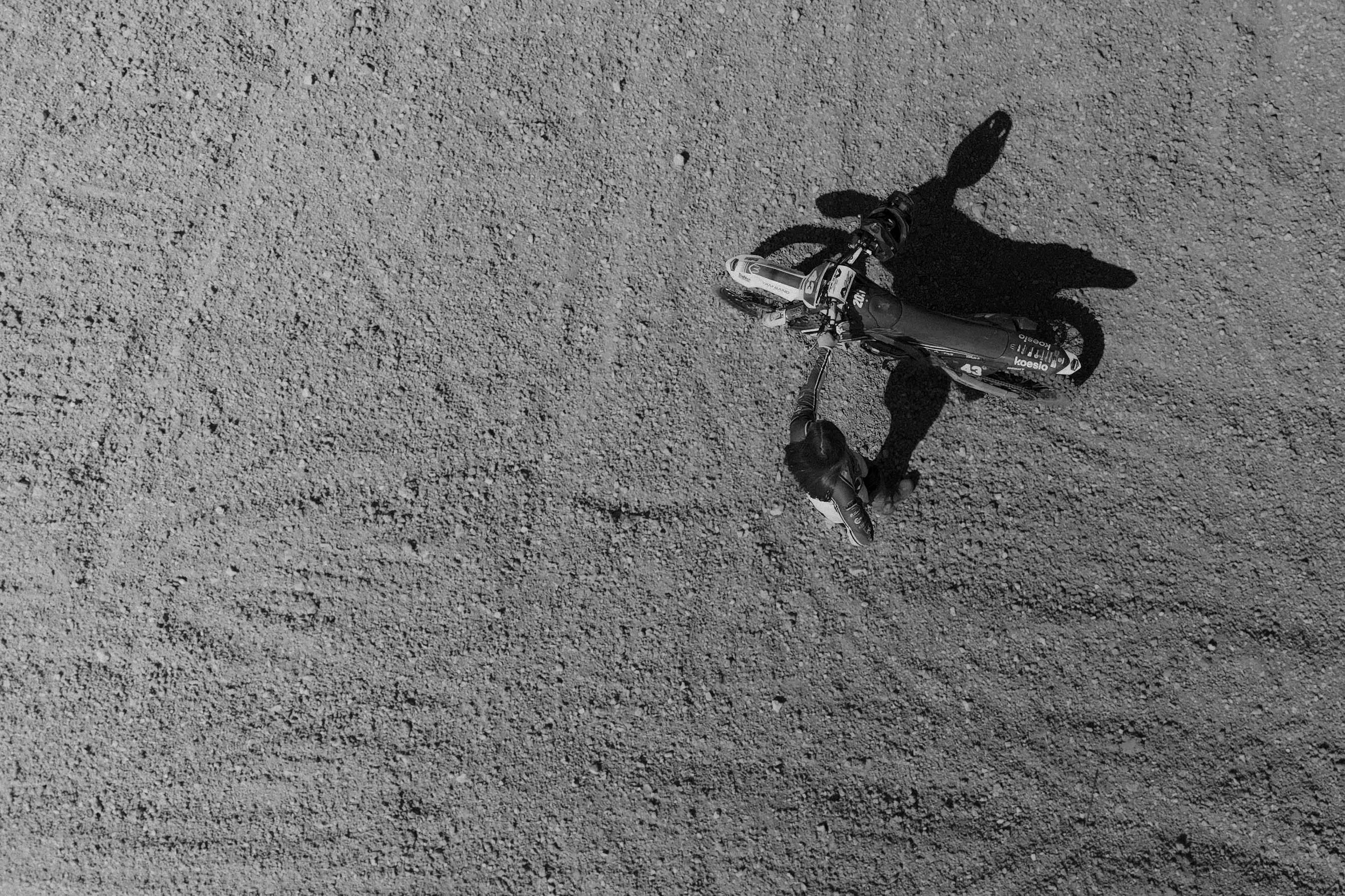 Vue aérienne d'une personne portant un casque de moto, à côté d'une motocross stationnée sur un sol composé de gravier. Issue d'une vidéo de sport du Studio Kroma pour le projet Limitless.