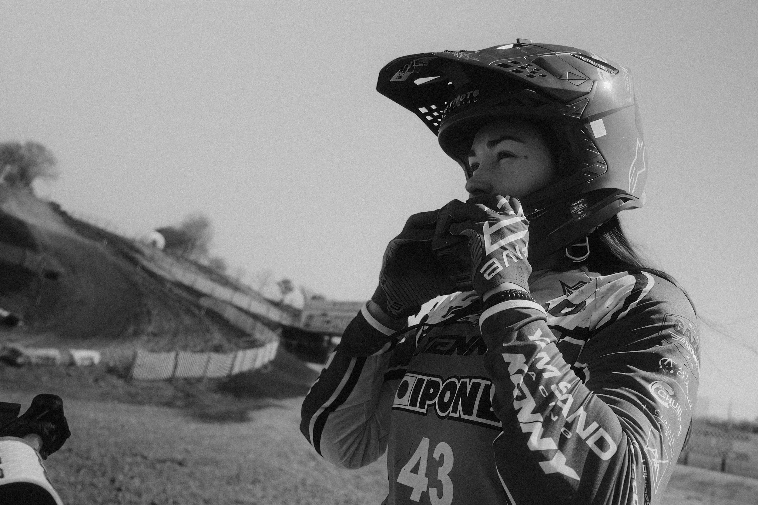 Une femme motocross portant un casque, des gants et un maillot de motocross, dans un environnement de course, en pleine préparation ou concentration. Issue d'une vidéo de sport du Studio Kroma pour le projet Limitless.