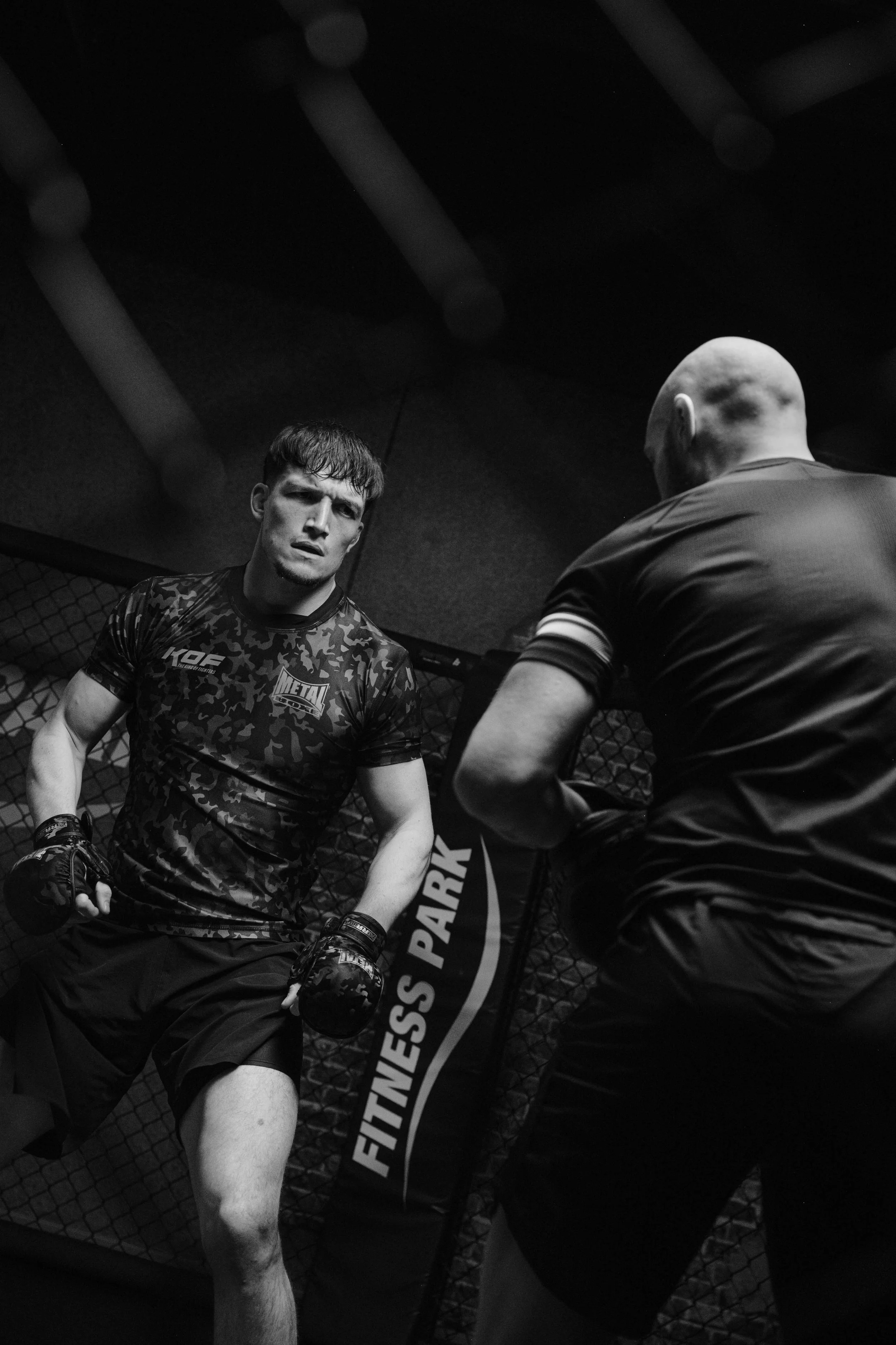 Deux hommes dans une cage de boxe, l'un portant des gants de boxe, en pleine séance d'entraînement ou de confrontation, dans une salle sombre. Issue d'une vidéo de sport du Studio Kroma pour le projet Limitless.