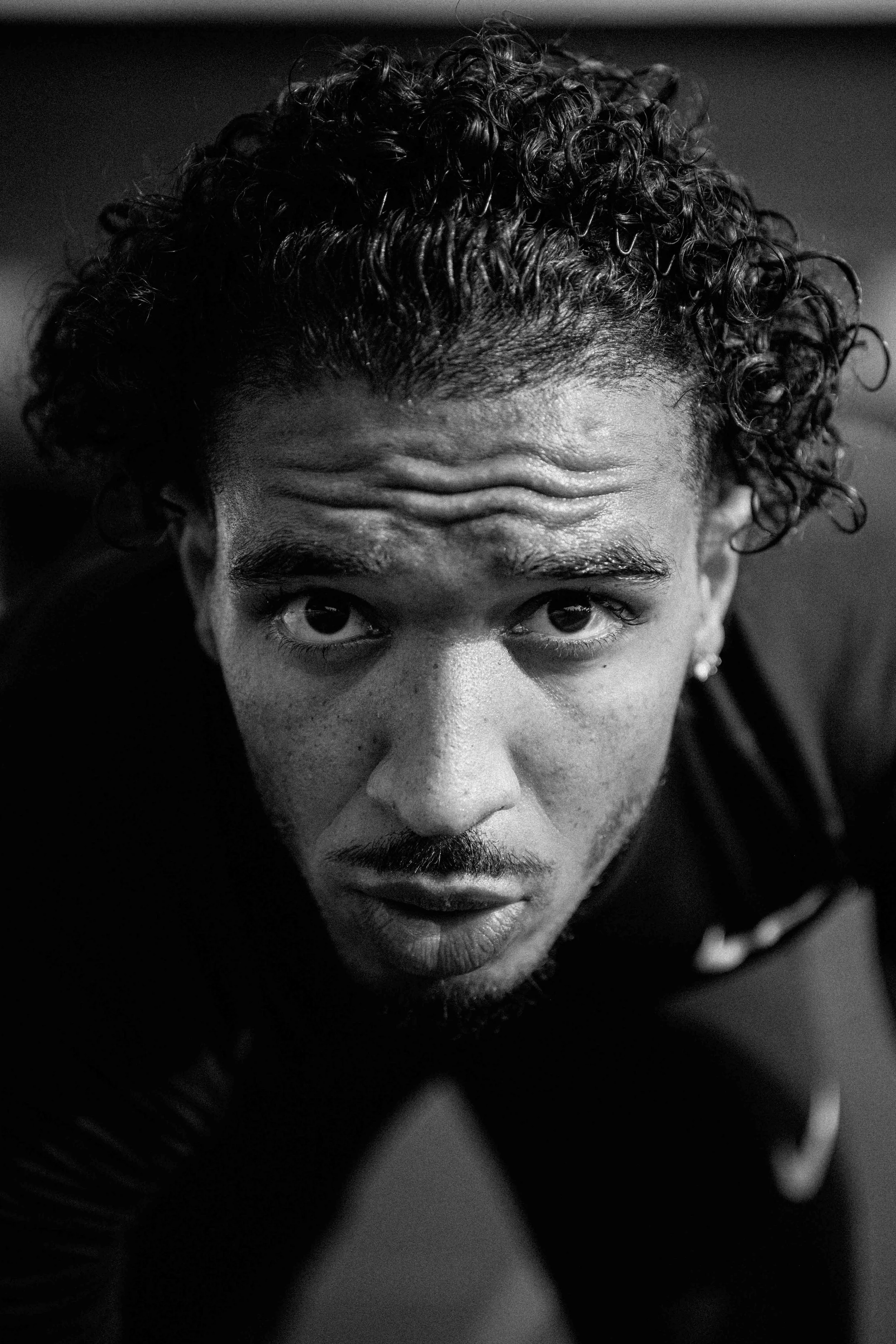 Portrait en noir et blanc d'un homme avec des cheveux bouclés, regardant vers l'objectif, dans une posture dynamique. Issue d'une vidéo de sport du Studio Kroma pour le projet Limitless.