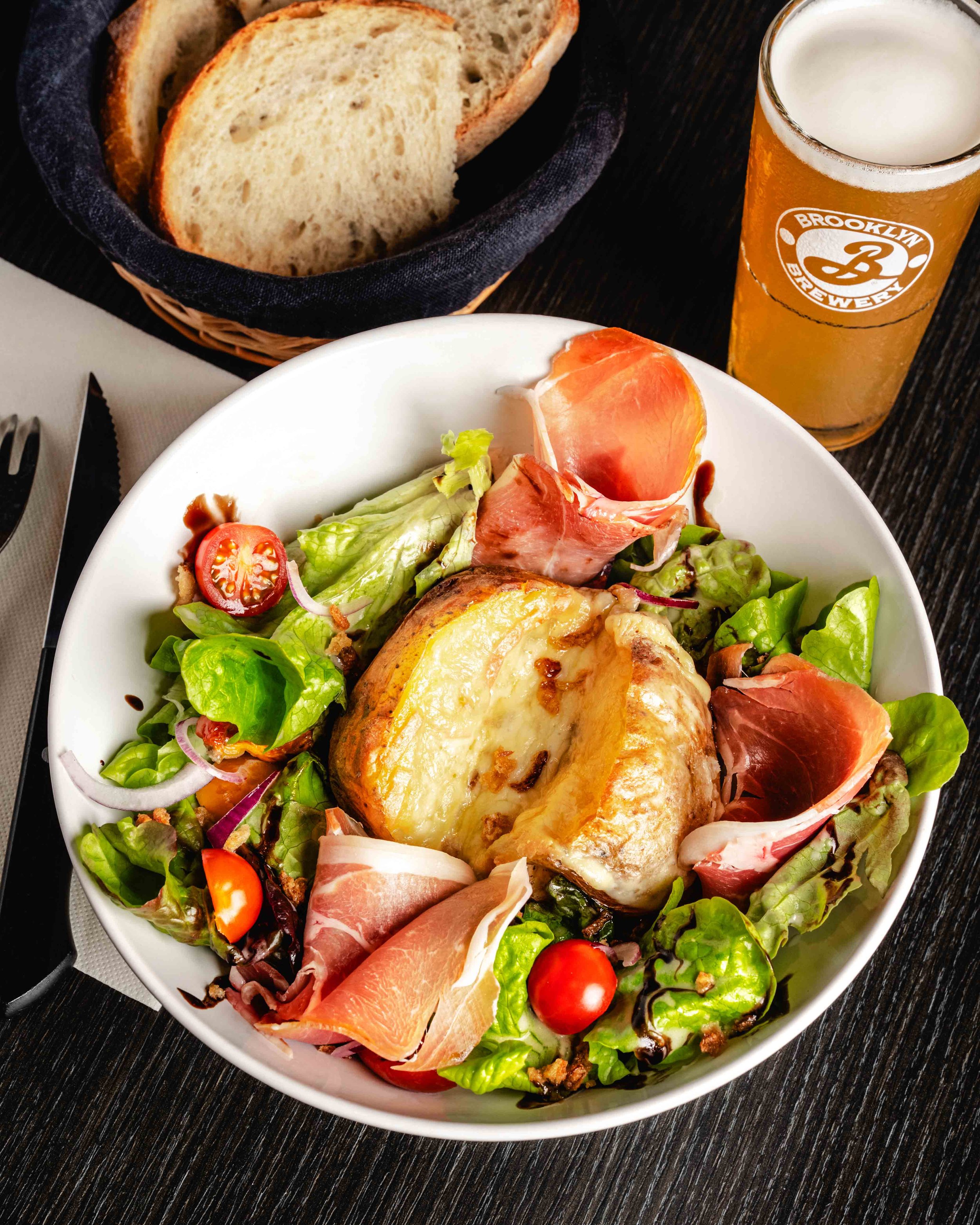 Salade avec fromage chaud, jambon, tomates cerises, et feuilles de laitue, accompagnée de pain et d'une bière.  Issue d'un projet de photo culinaire du Studio Kroma pour le restaurant L'Eden Bowl.