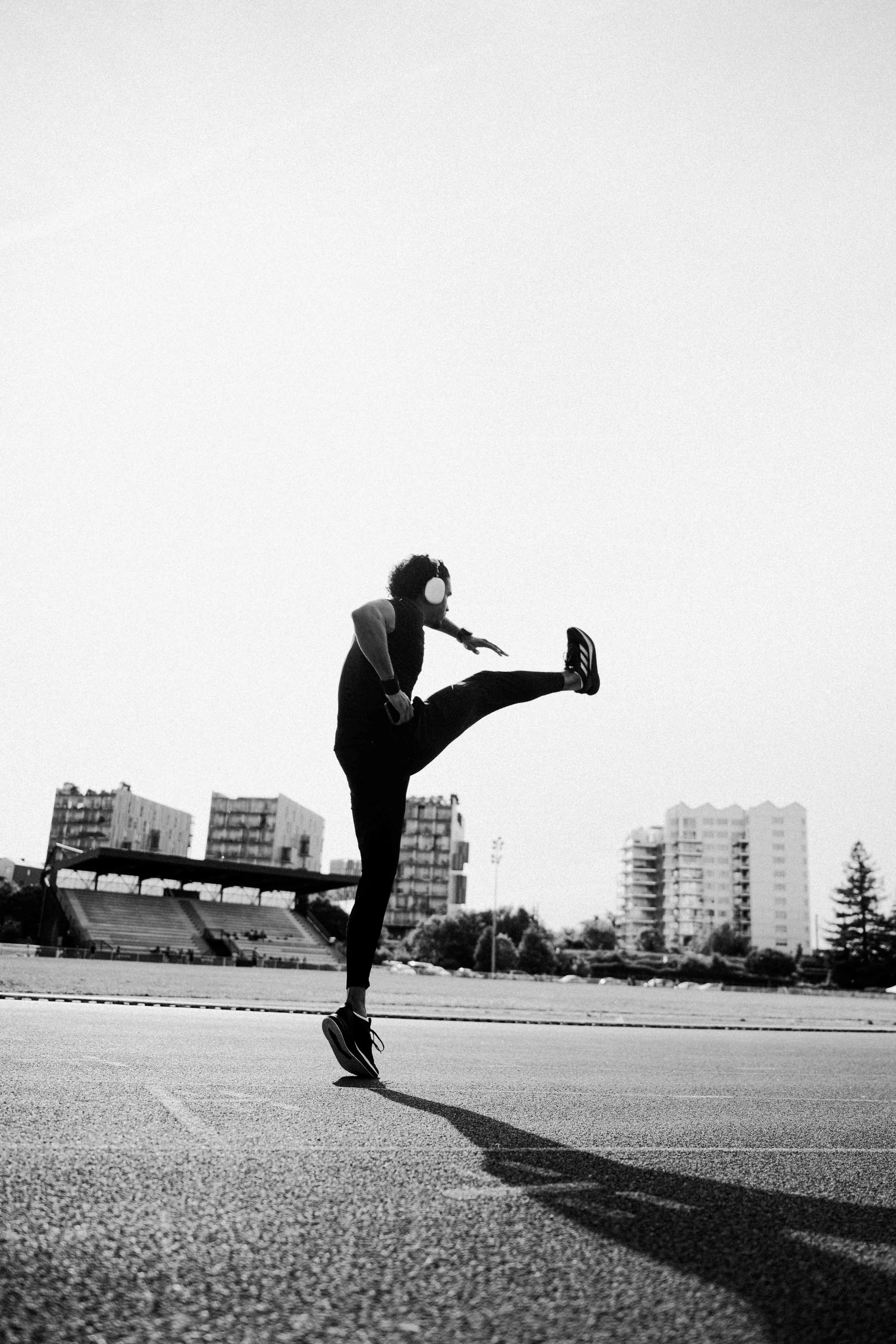 Une personne portant des écouteurs, en plein échauffement sur une piste d'athlétisme, avec des bâtiments en arrière-plan, en noir et blanc. Issue d'une vidéo de sport du Studio Kroma pour le projet Limitless.