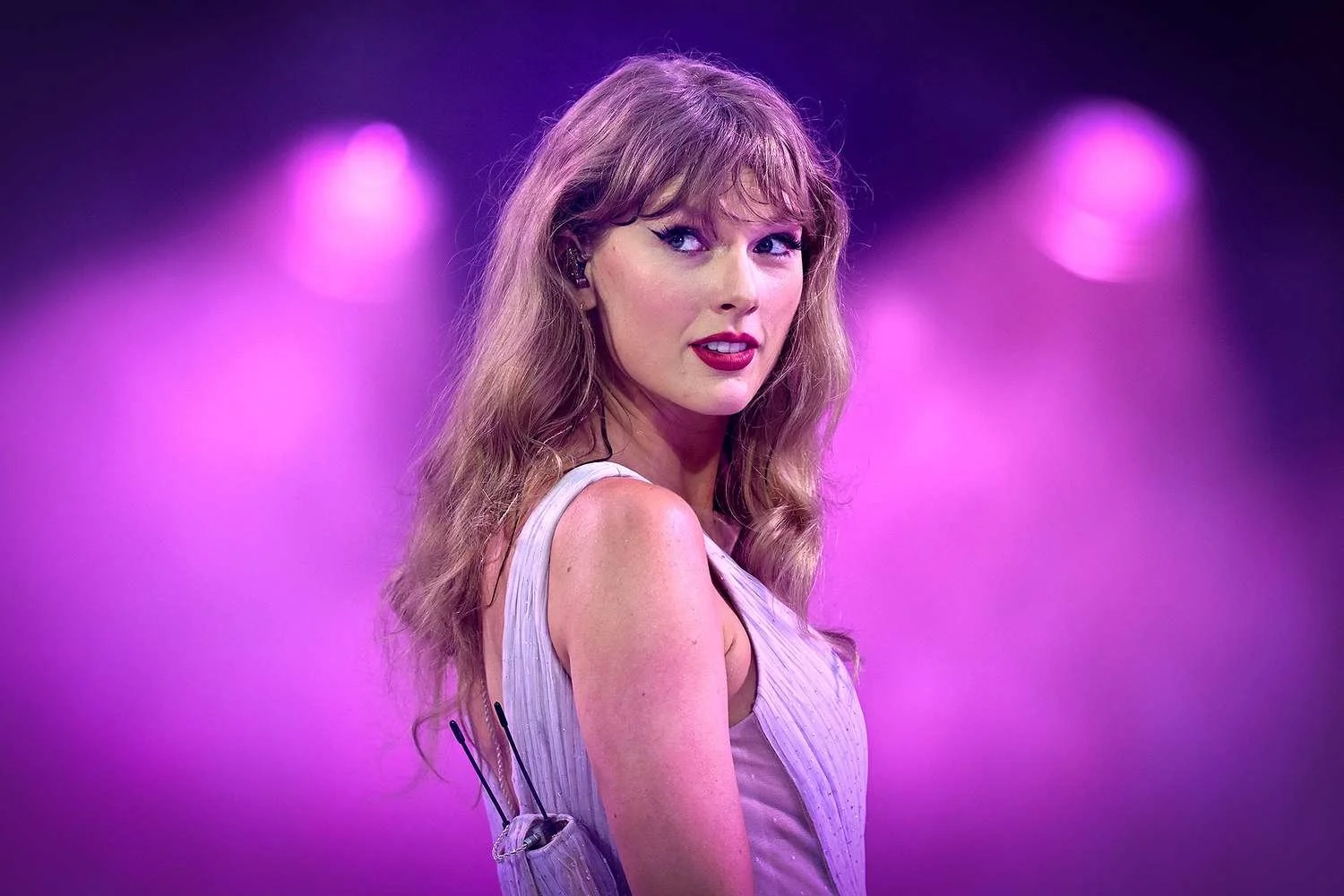 Taylor Swift performing on stage with purple lighting, wearing a light-colored dress.