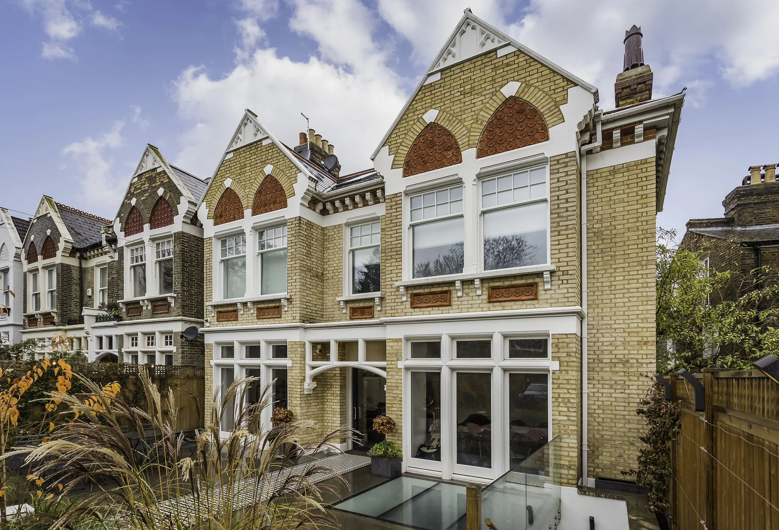 A row of Victorian-style brick houses with decorative gables and large windows. Walk on glass, new basement.