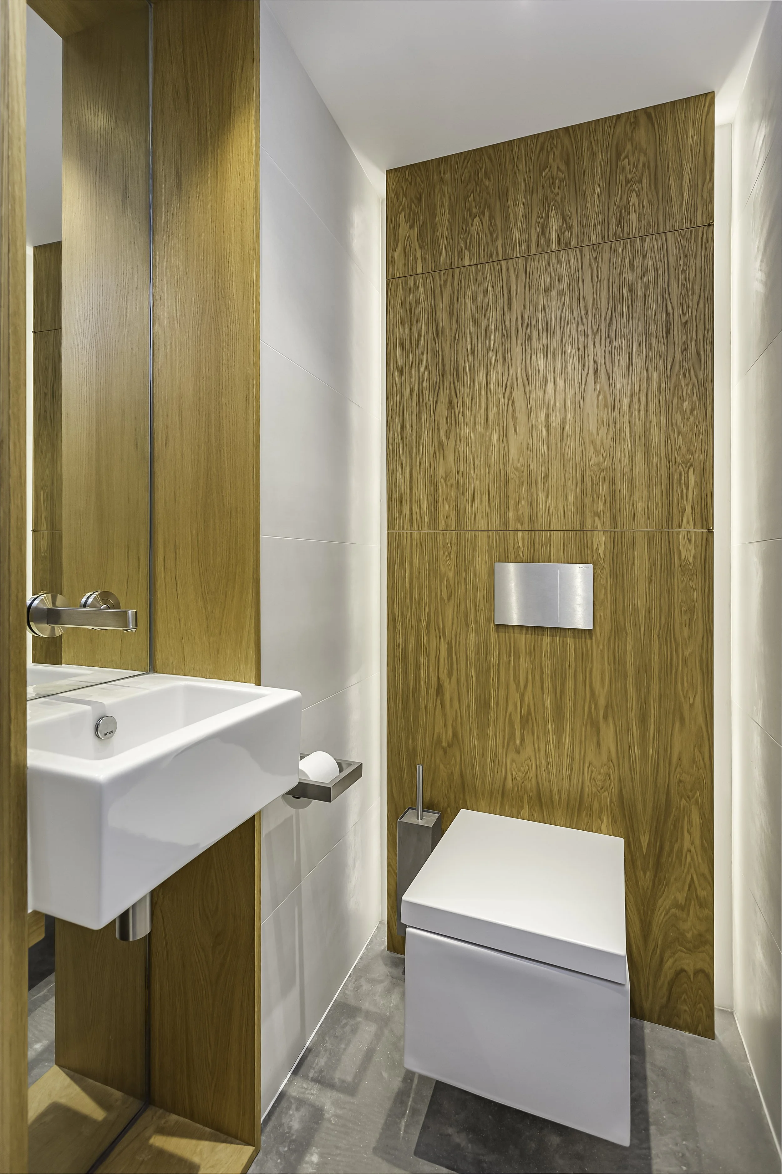Modern small bathroom with white tile walls, wooden panel accents, a white toilet, and a small white sink with a mirror above.