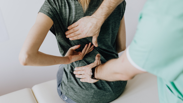 Woman in a grey t-shirt showing her doctor where the pain in her back is