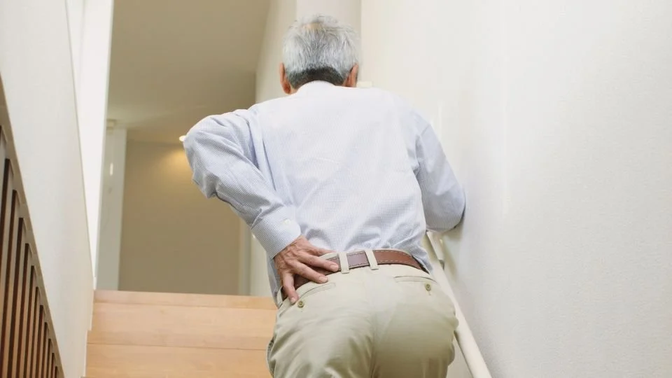Older man walking up the stairs clutching his hip experiencing sciatica pain