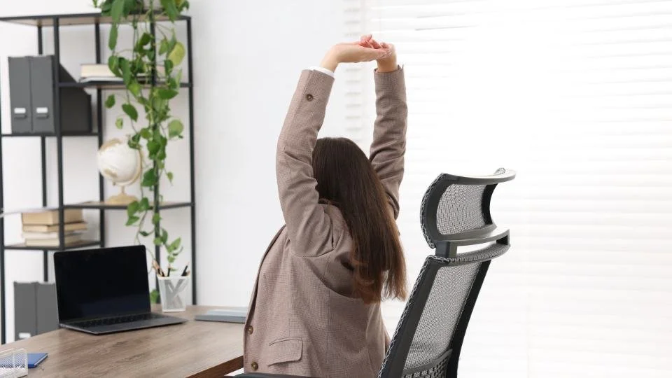 “Woman stretching while seated at a desk, illustrating mobility and back care before spinal fusion surgery.