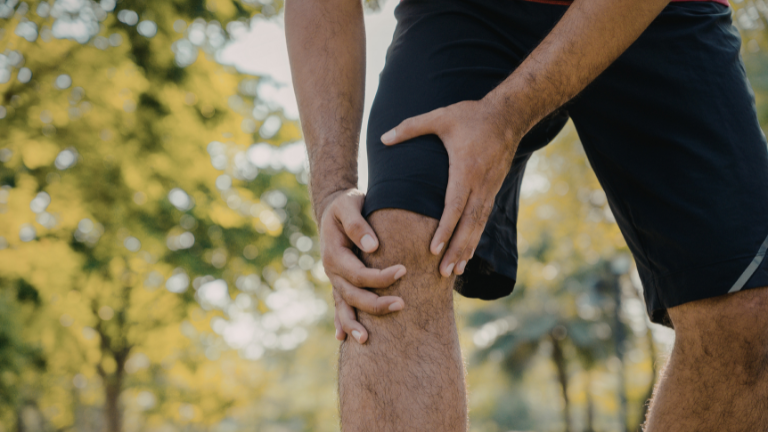 Man in black shorts holding his knee in a park