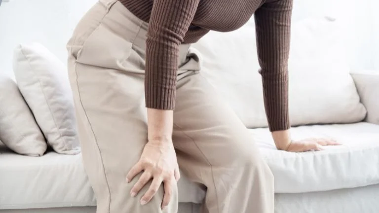 Individual experiencing difficulty standing due to lower back pain, a symptom linked to spinal conditions