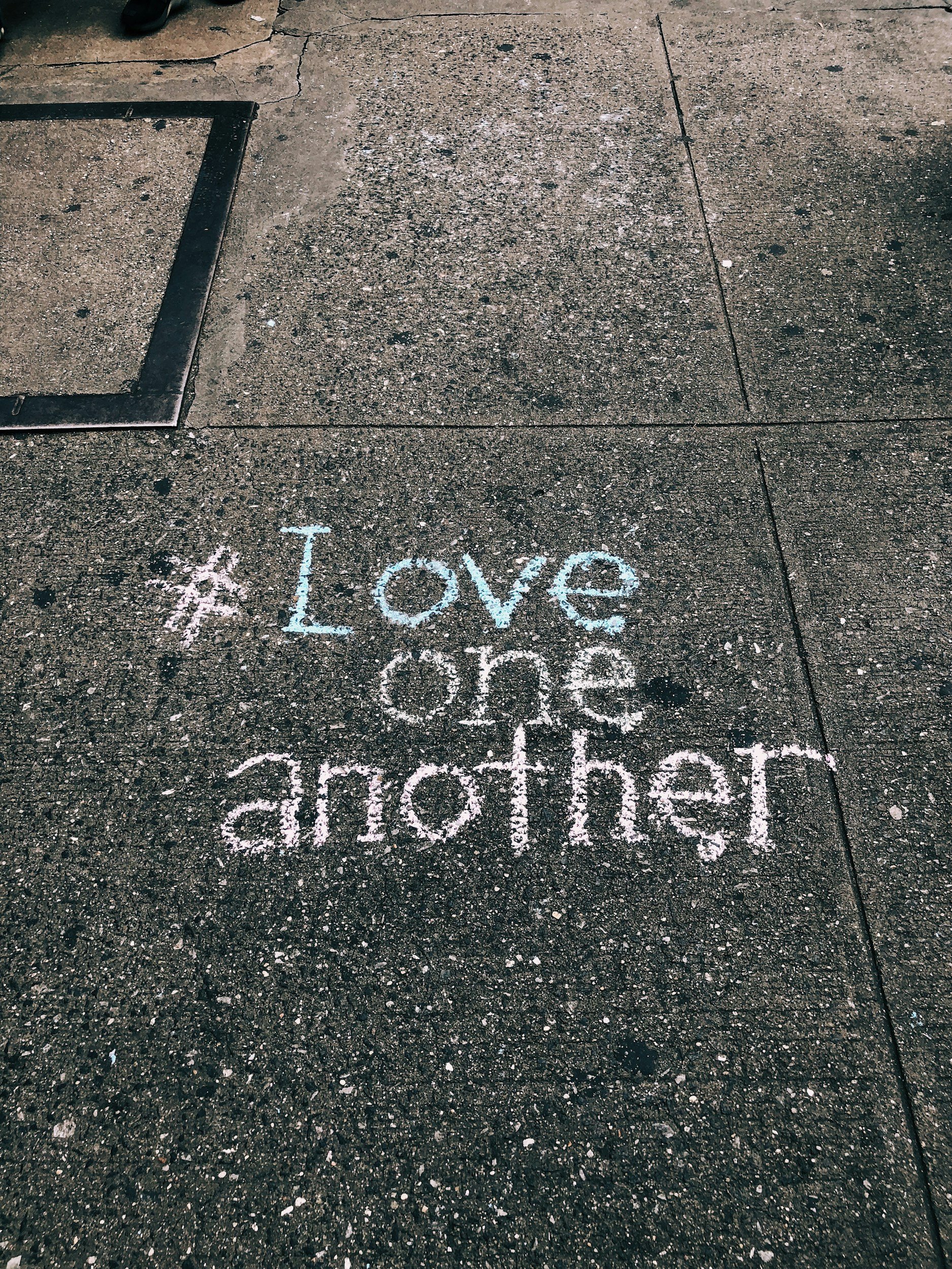 Colorful sidewalk chalk writing of the word "Love" and partially visible words on a concrete sidewalk.