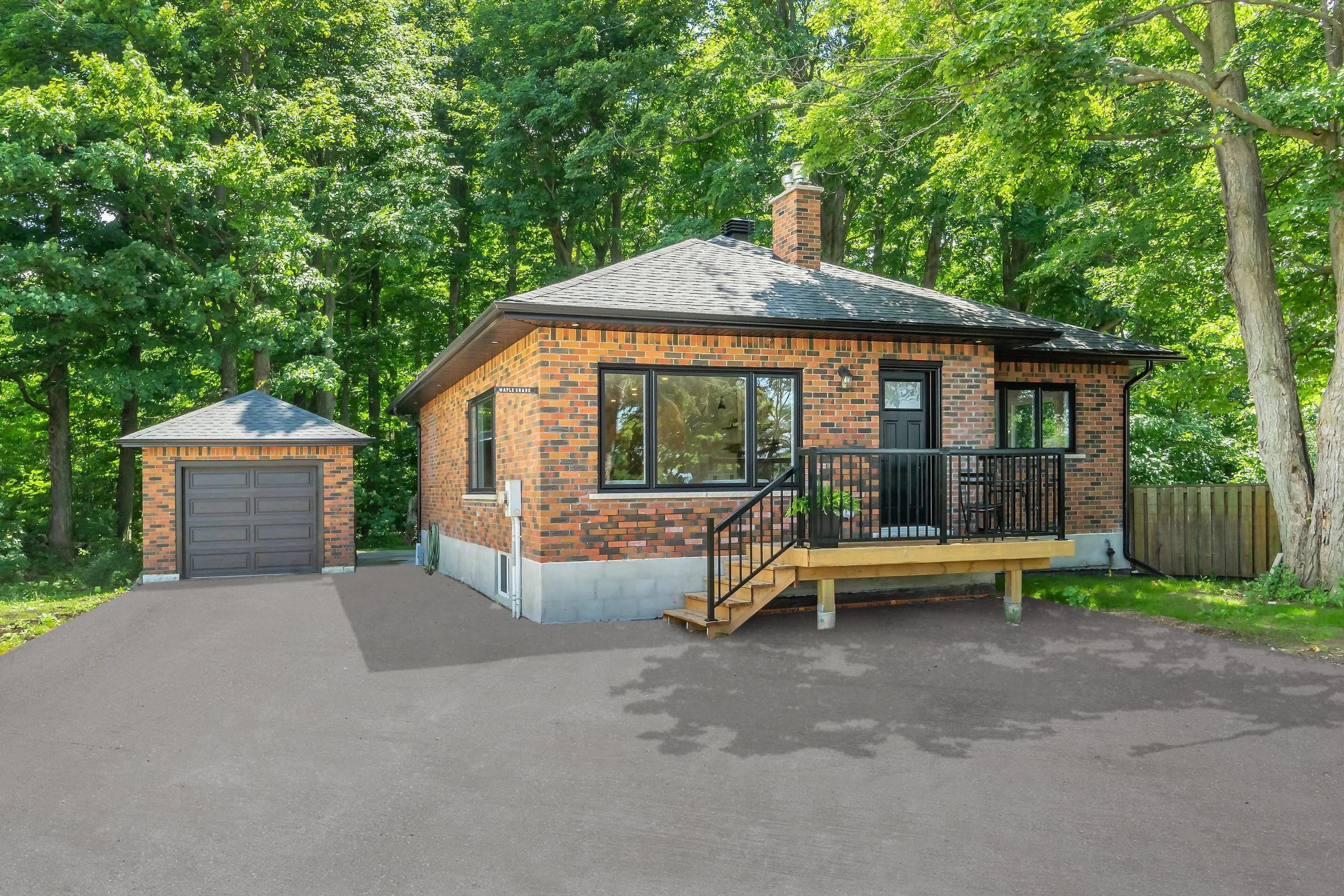Small brick house with black door and windows, surrounded by trees, with an attached garage and a paved driveway.