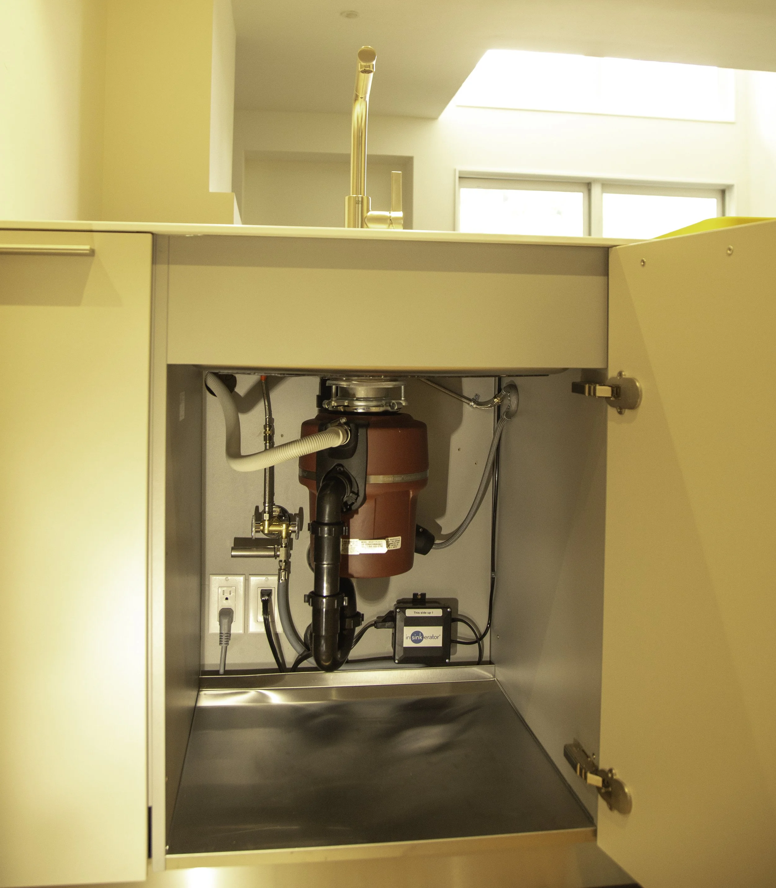 Open kitchen cabinet with reverse osmosis water filtration system, including a red filter unit, plumbing pipes, and an electronic control box, beneath a sink with a modern faucet.