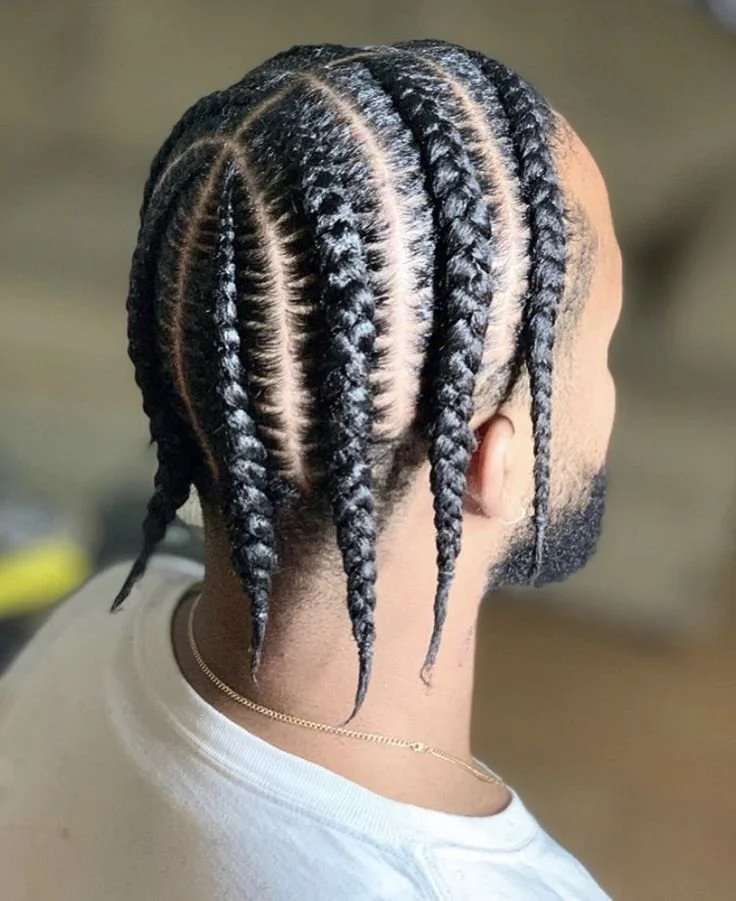 Person with cornrows hairstyle, rear view, wearing a white shirt and necklace.