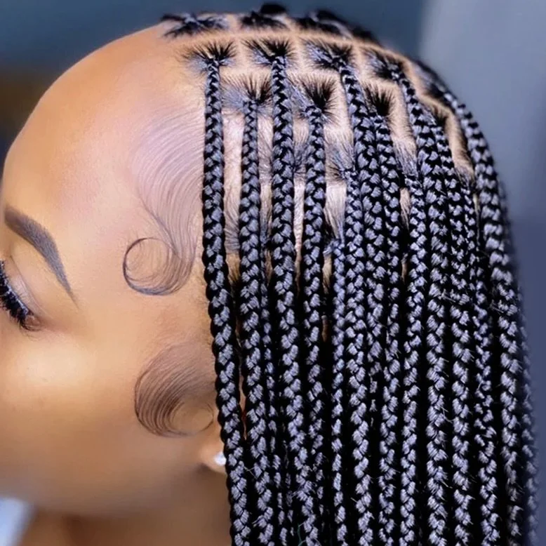 Person with intricate cornrow braids against a green leafy background.