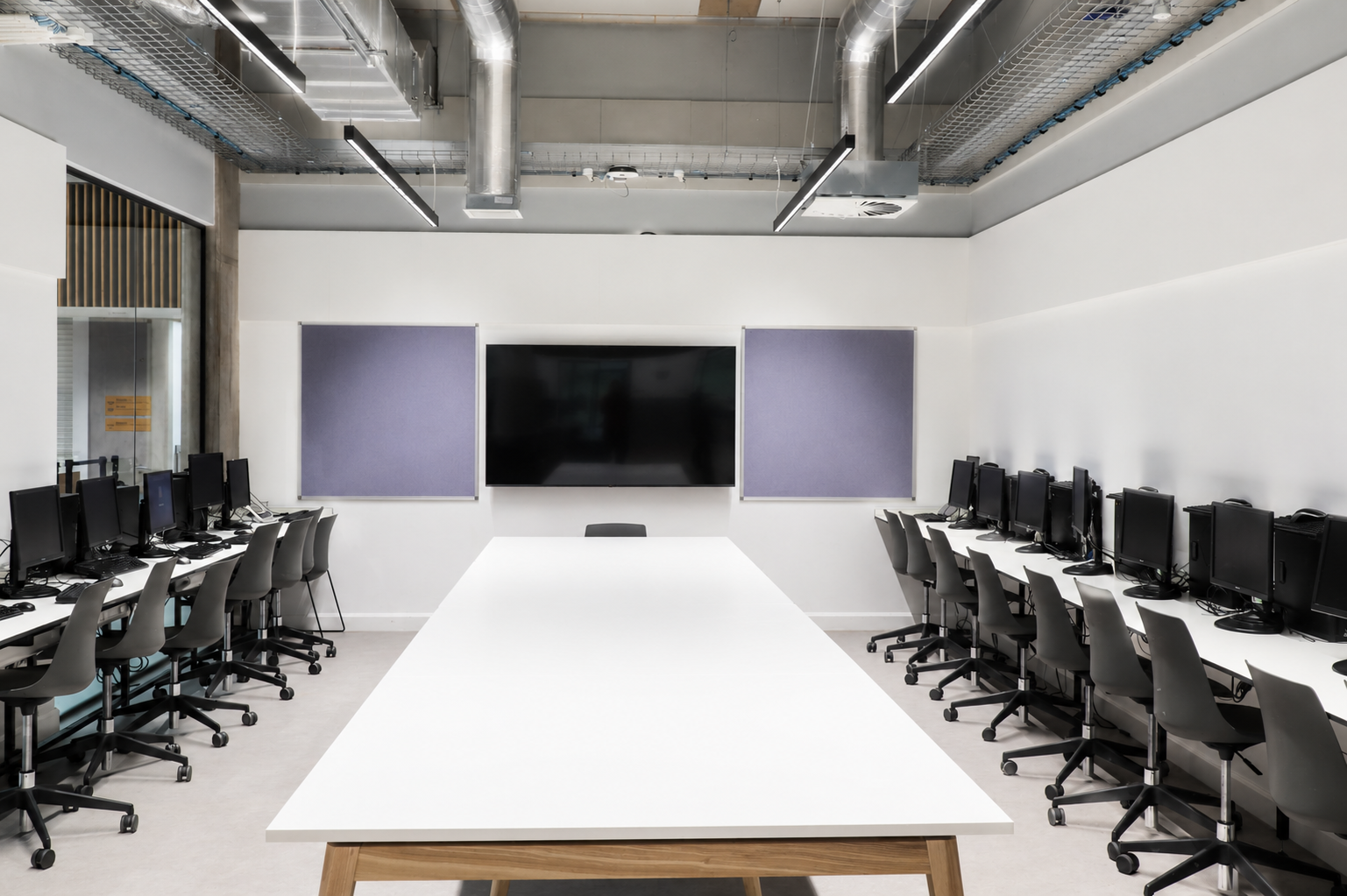 ICT classroom at Peebles High School featuring fitted computer workstations, office chairs, a central table, display screen and pinboards.