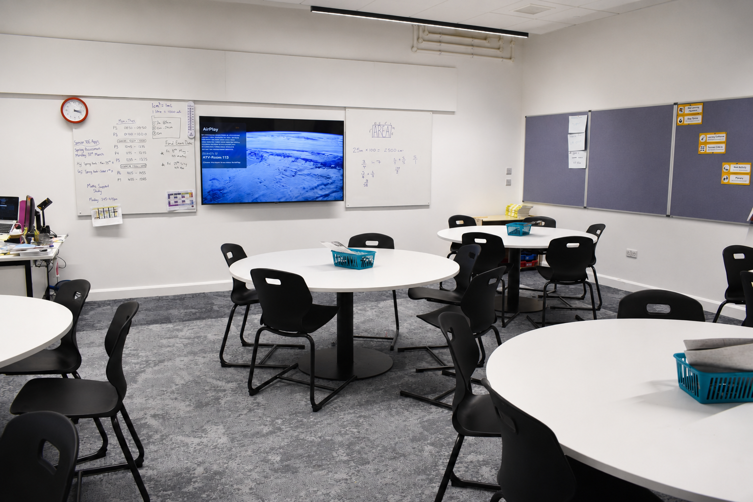 Modern classroom at Peebles High School featuring circular tables, black chairs, whiteboards, display screens and wall-mounted pinboards.