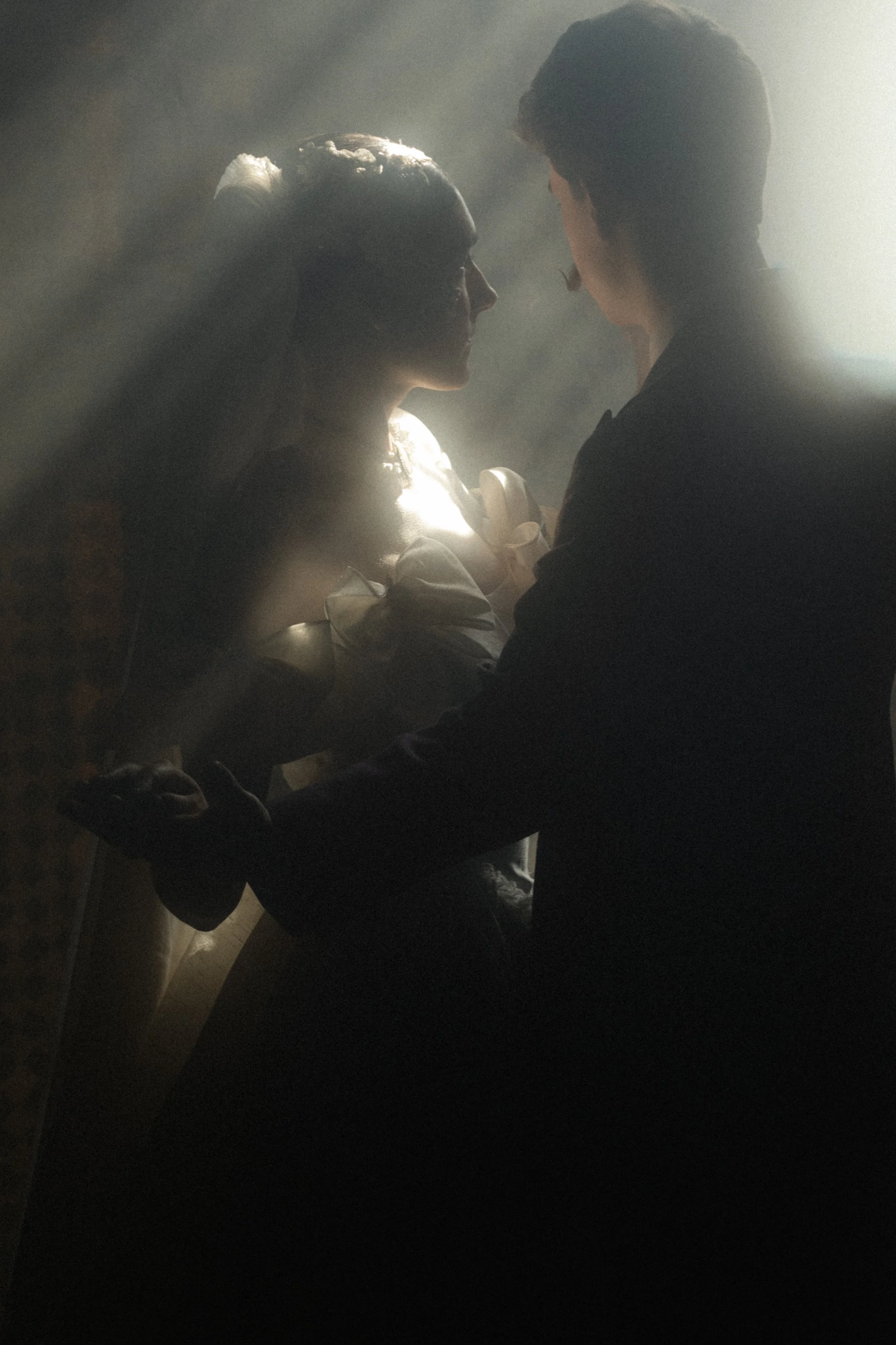 A man and a woman face each other closely in a foggy or smoke-filled environment with backlighting, creating a silhouette effect.