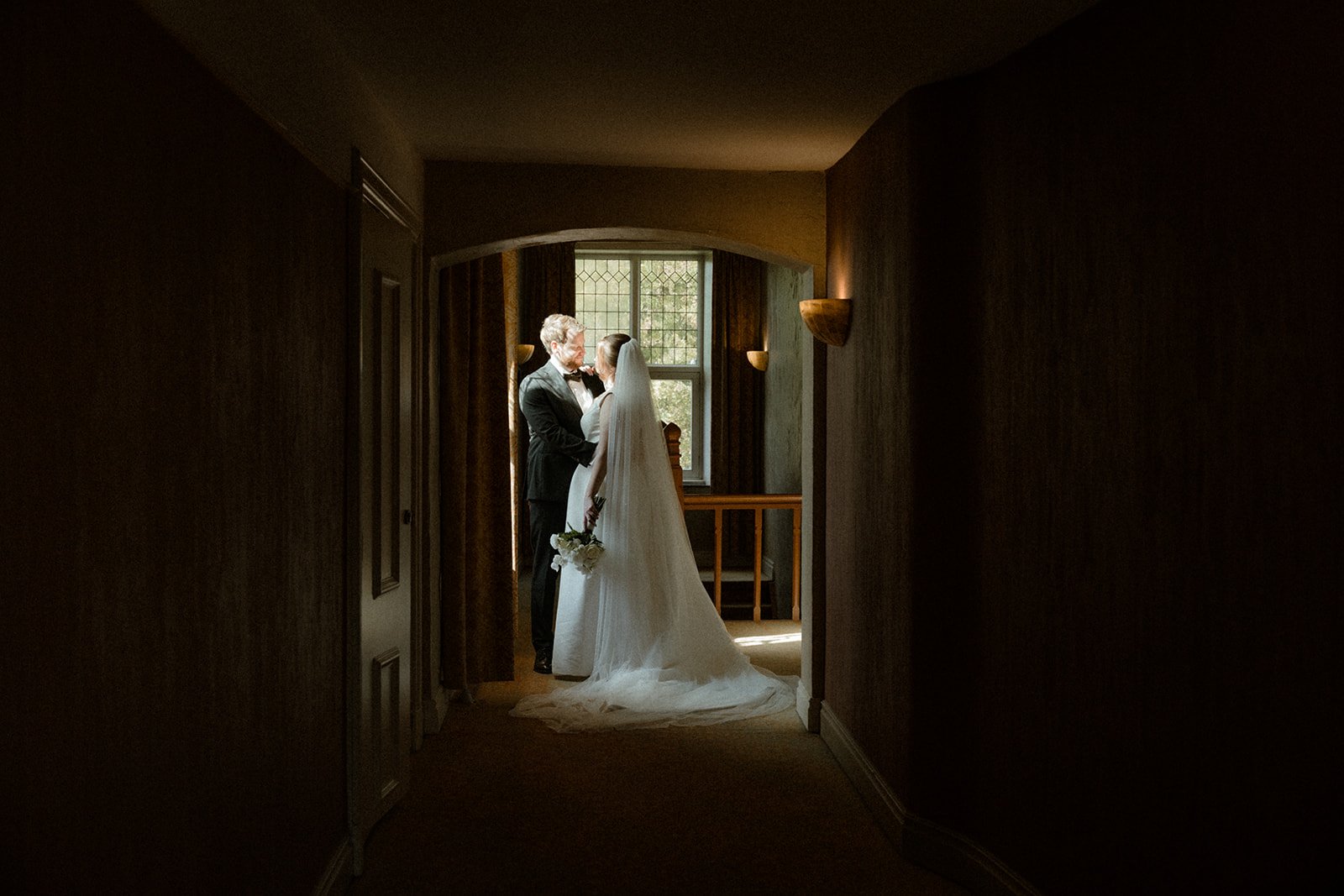 Een bruid en bruidegom in een helder verlichte kamer, verliefd kijkend naar elkaar, met een raam op de achtergrond. Huwelijkskleding, de bruid in een wit jurk met sluier en de bruidegom in een zwart pak.