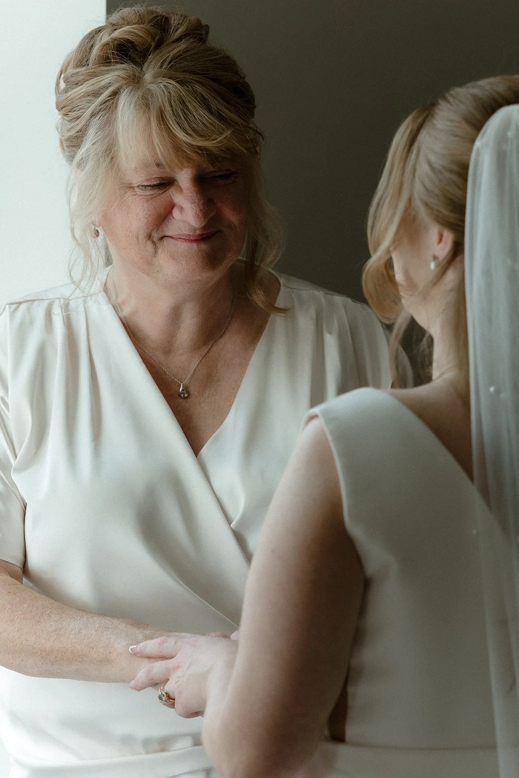Vrouw in witte jurk die haar dochter steun en troost biedt aan haar bruiloft, met een zachte glimlach.