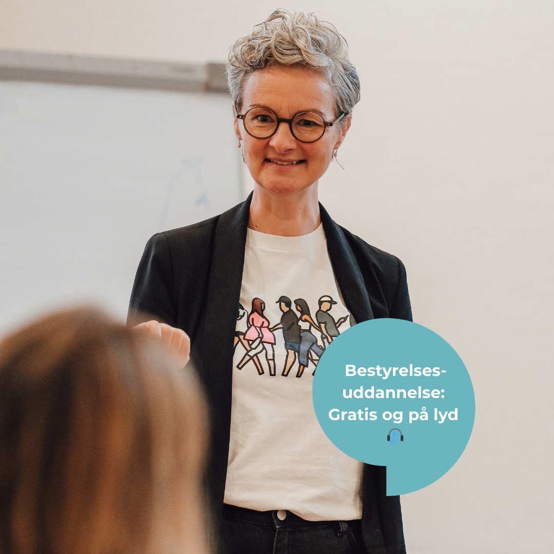 Foto fra bestyrelsesuddannelse med underviser, der taler til en deltager, der lytter