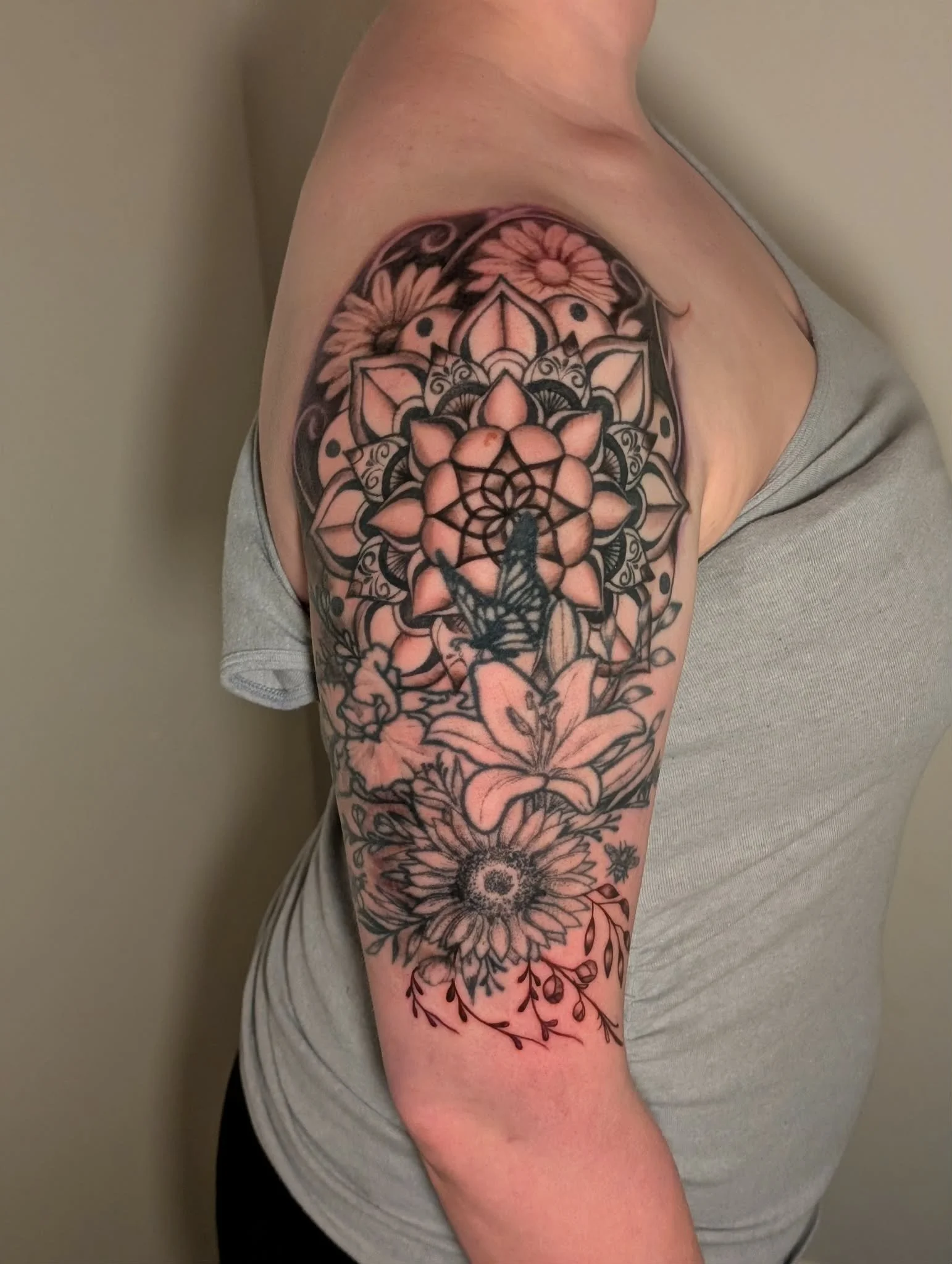 A person's upper arm featuring a large, detailed black and pink floral tattoo with various flowers and leaves.