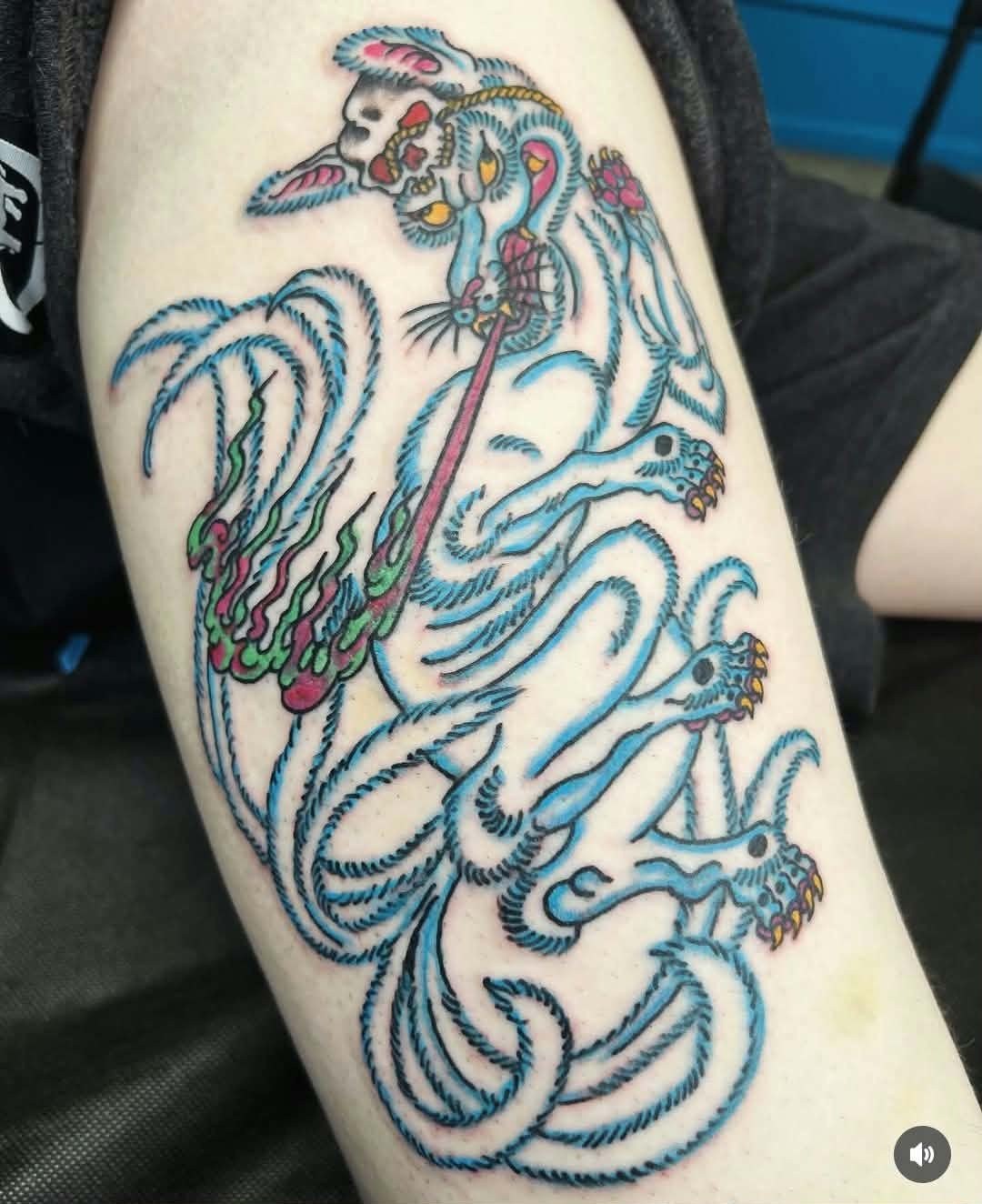 Colorful tattoo of a dragon with a stylized skull in its mouth, featuring blue, pink, green, and yellow ink, on a person's arm.