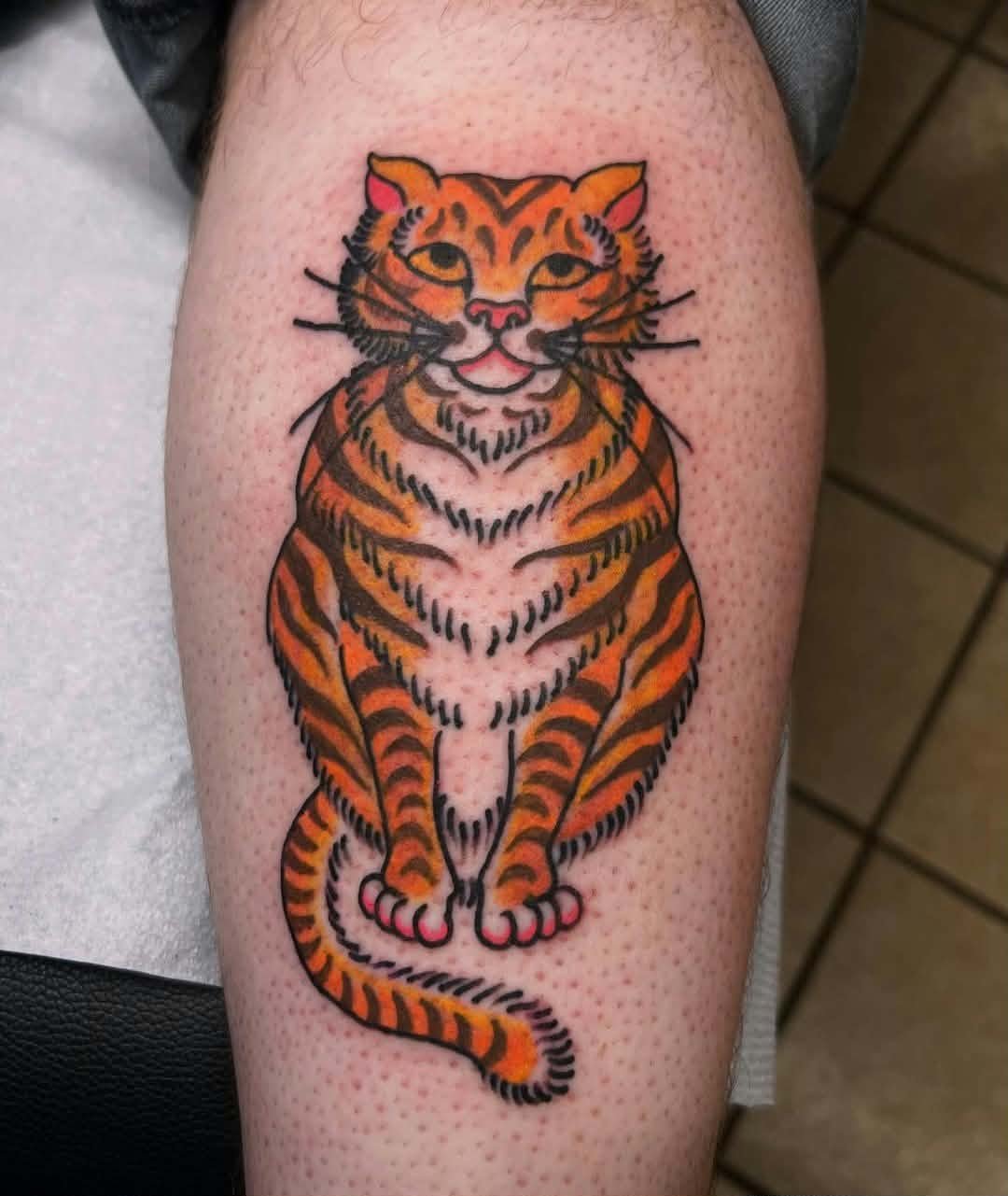 Colorful tattoo of a sitting tiger with orange and black stripes on a person's arm.
