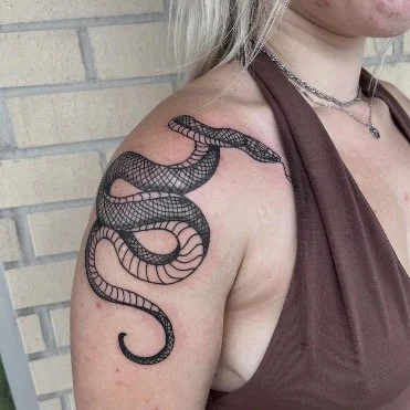 Shoulder cap black tattoo in fine-line with soft black and gray shading of a snake on a women’s shoulder 