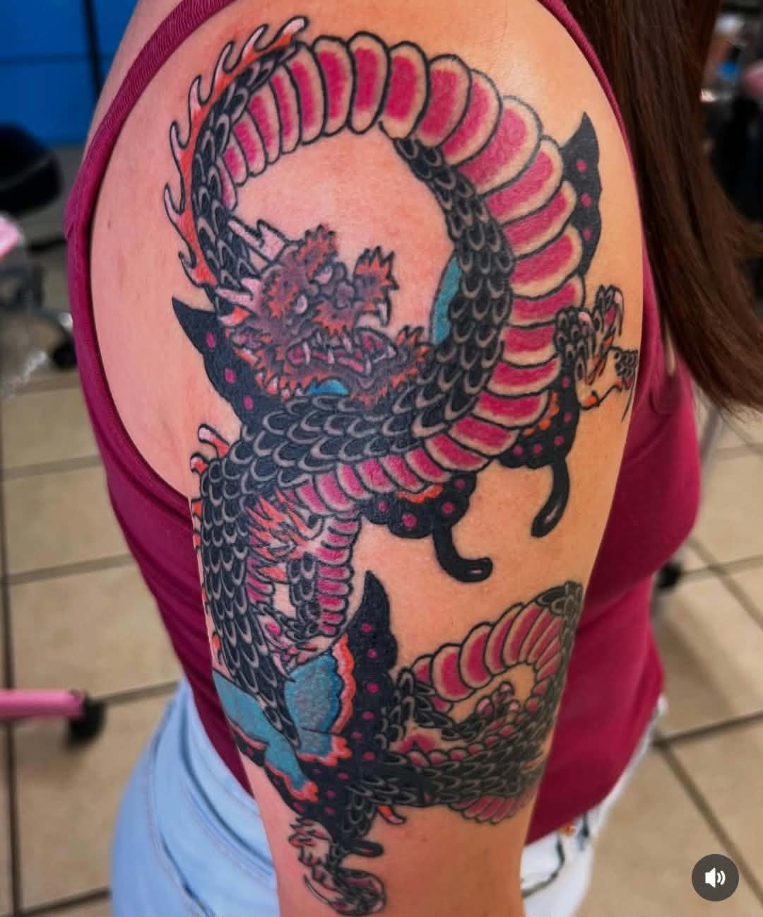 Colorful traditional Japanese dragon tattoo on person's upper arm featuring black, pink, and blue ink.
