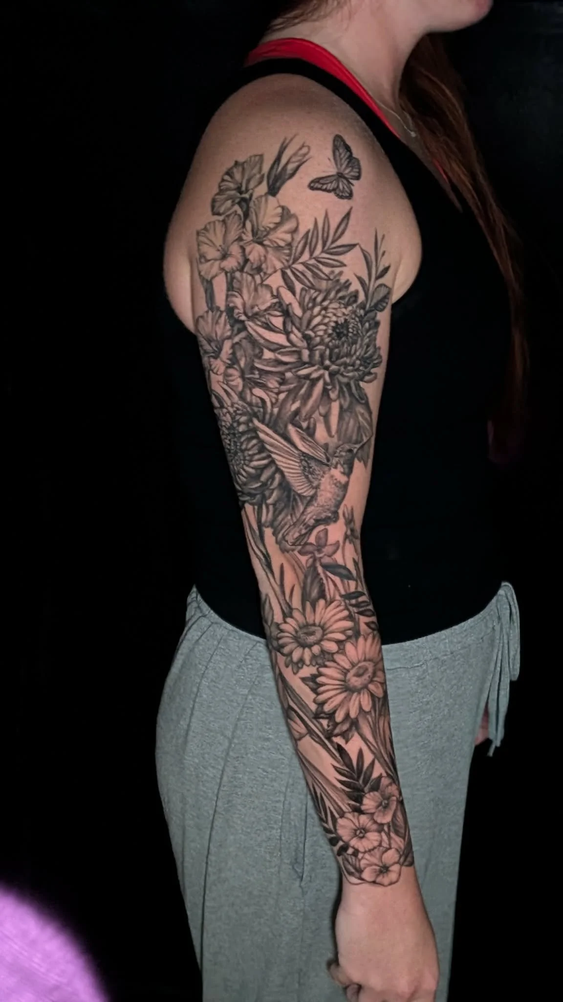 A woman with a full arm tattoo featuring flowers, leaves, a bird, and a butterfly.