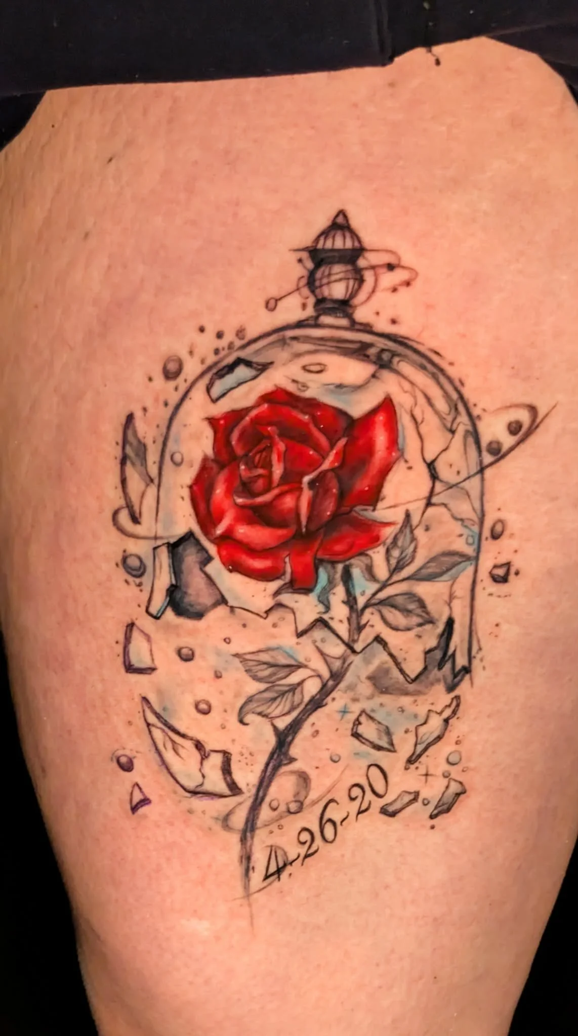 Tattoo of a red rose with geometric and abstract elements, surrounded by scattered dots and fragments. The tattoo also features dates and a prominent camera illustration.