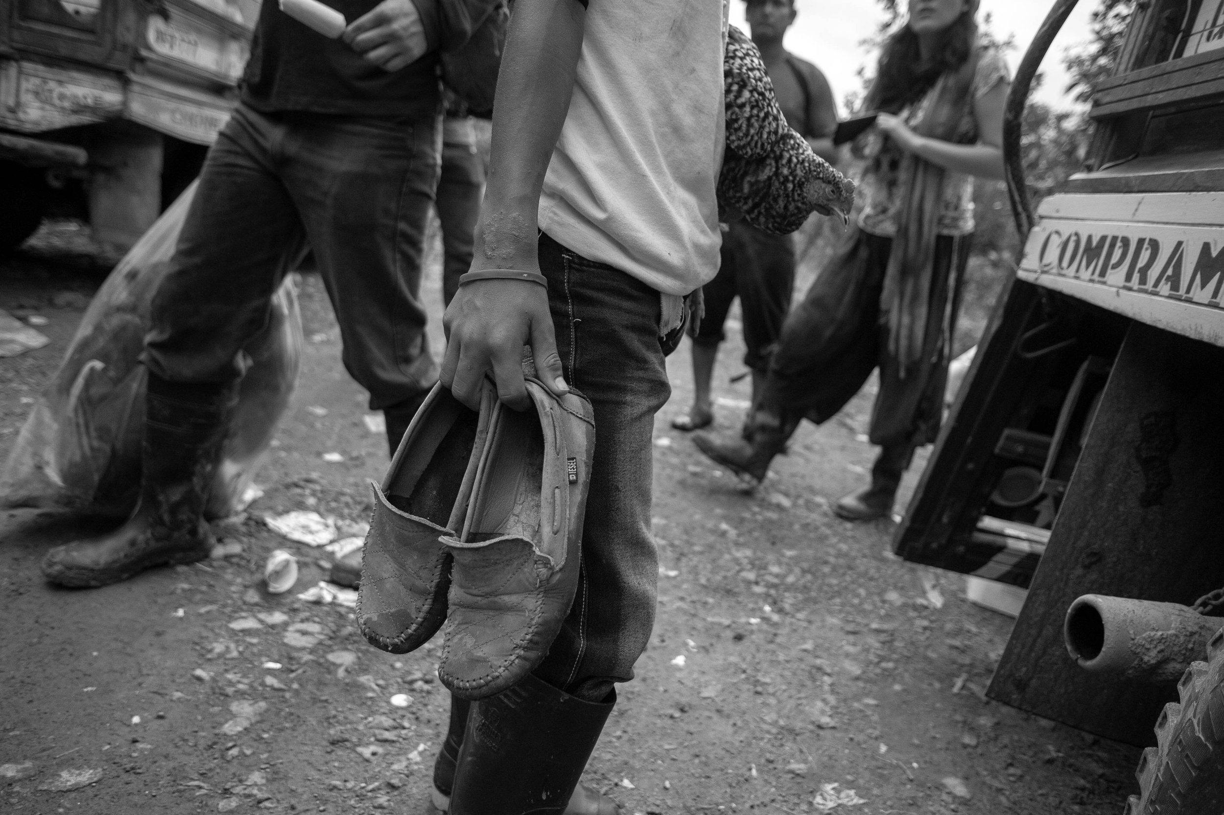 A person holding a pair of slippers in a busy outdoor market, surrounded by people and market stalls.