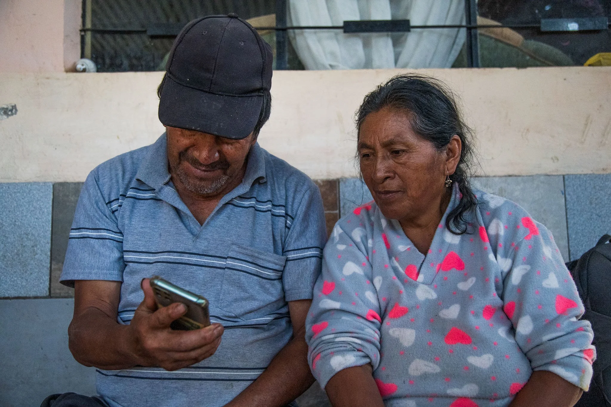 An elderly man and woman sitting together, looking at a smartphone.