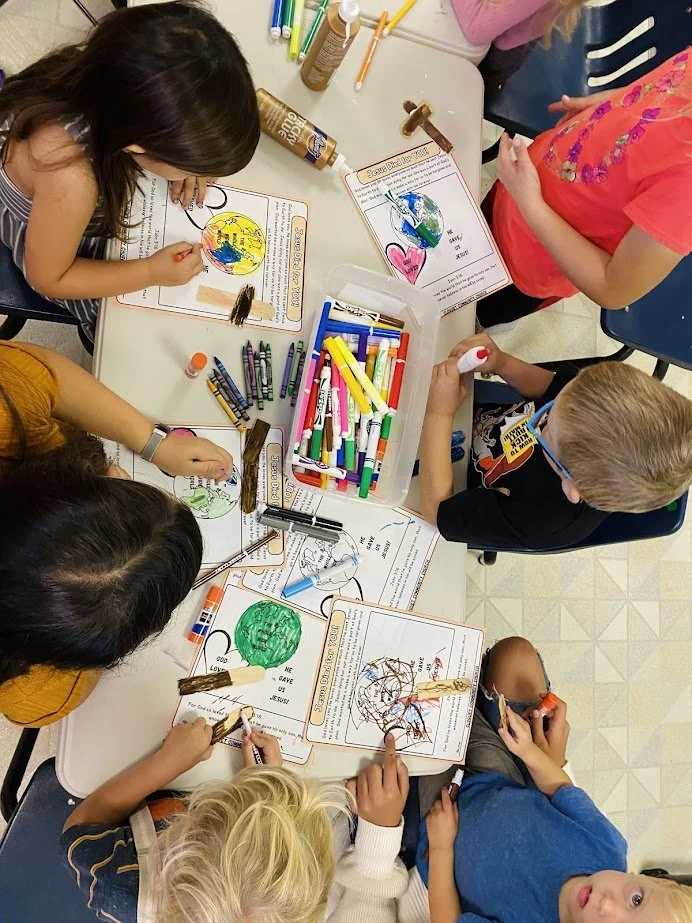 Children at a table coloring and decorating sheets with crayons, markers, and craft supplies.