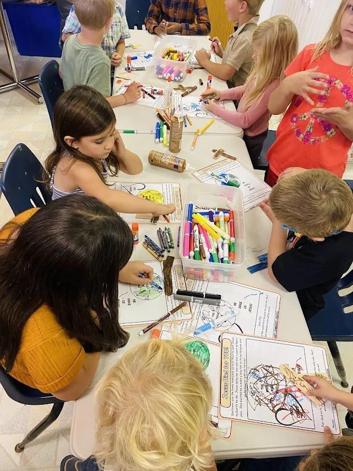 Children engaging in arts and crafts activity at a table, using markers, crayons, and coloring pages.