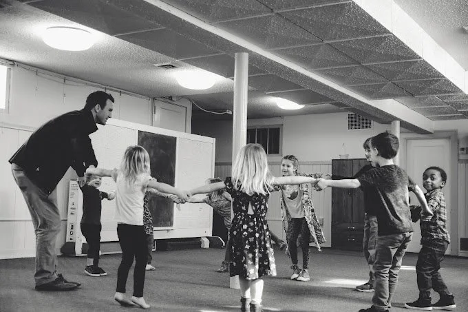 Children and a teacher playing a group game in a room.