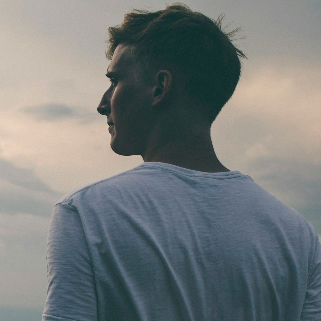 Side profile of a young man in a white shirt outdoors during dusk or dawn.