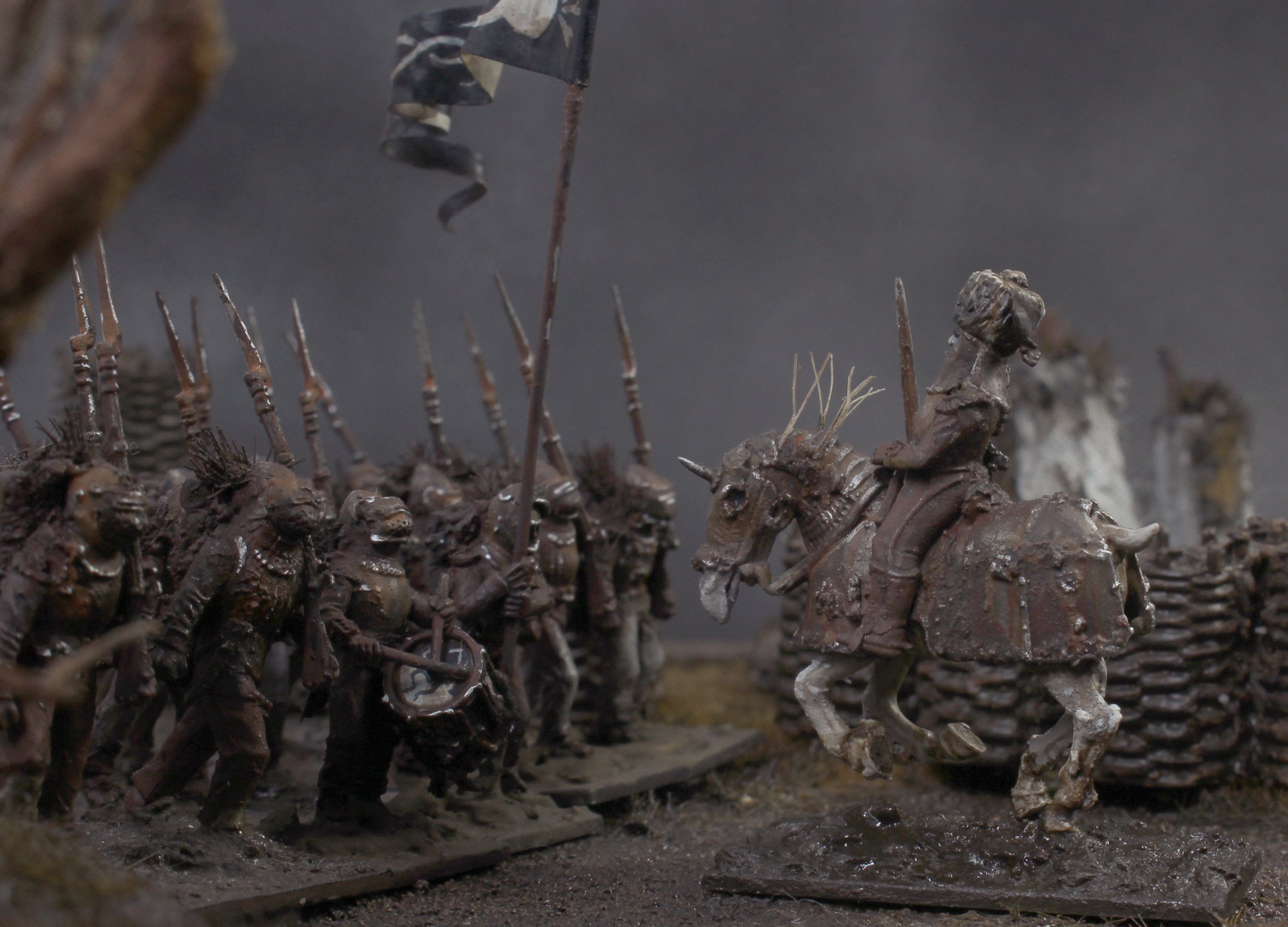 Miniature metal figurines of medieval soldiers and a knight on horseback in formation, with shields and spears, set in a diorama scene.