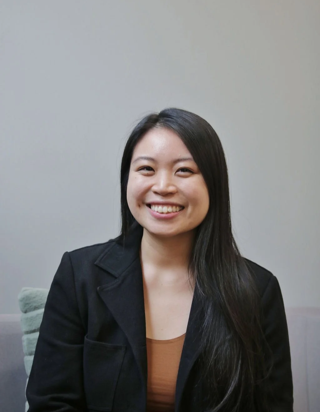 Asian woman wearing a black blazer and brown top smiling at camera