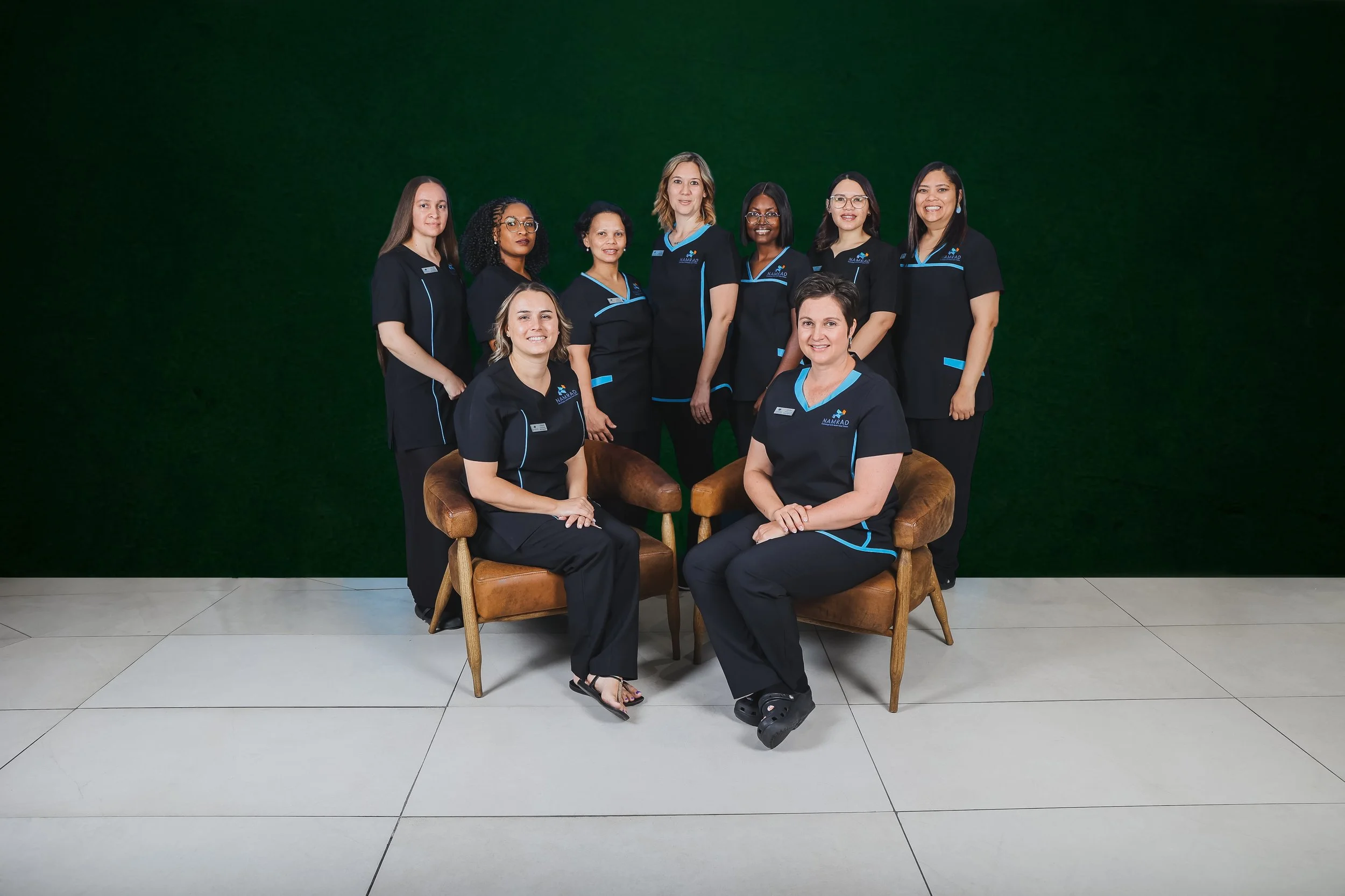 Group of six women in black uniforms, smiling in front of a dark green background.