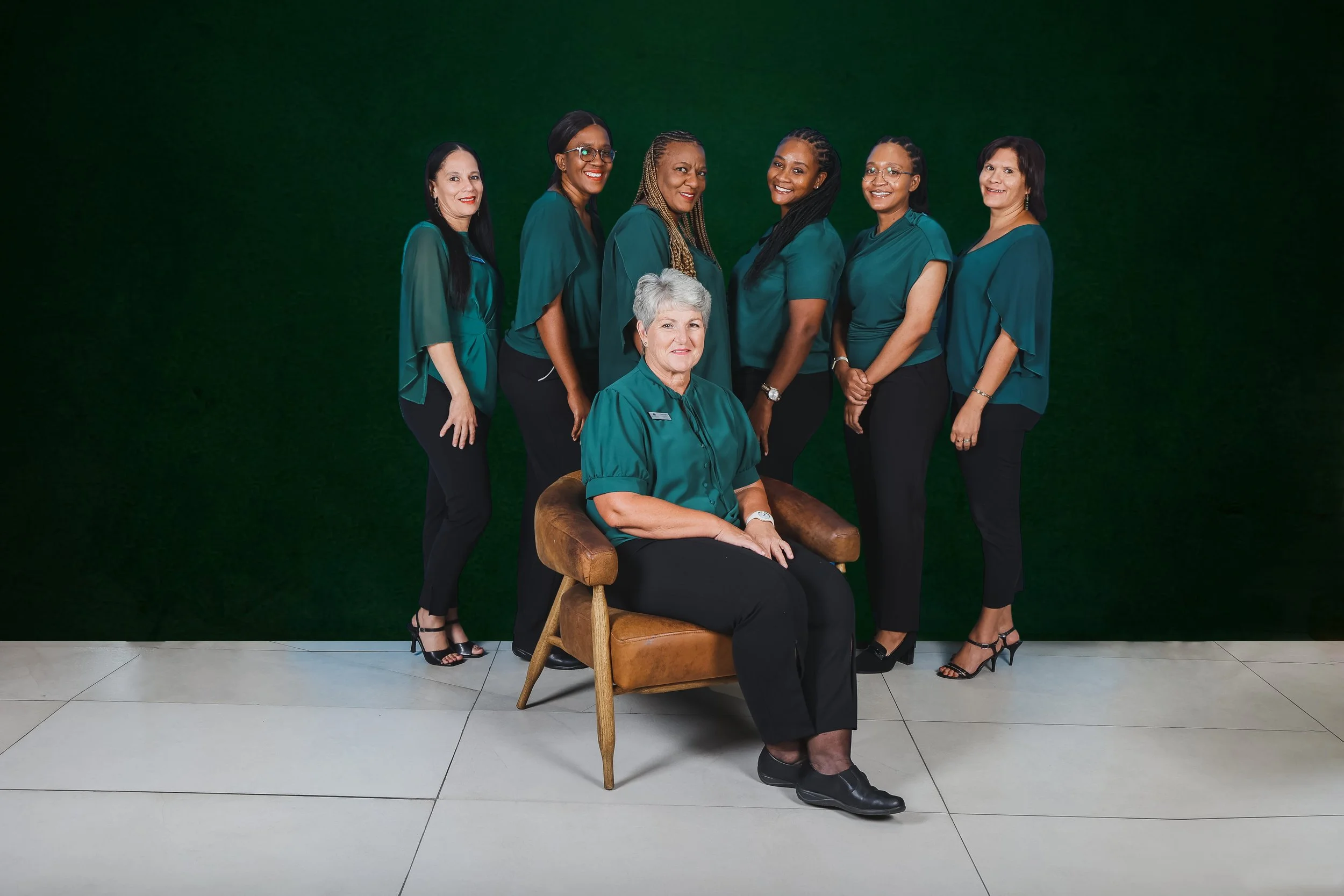Seven ladies in front of a green wall wearing green and black